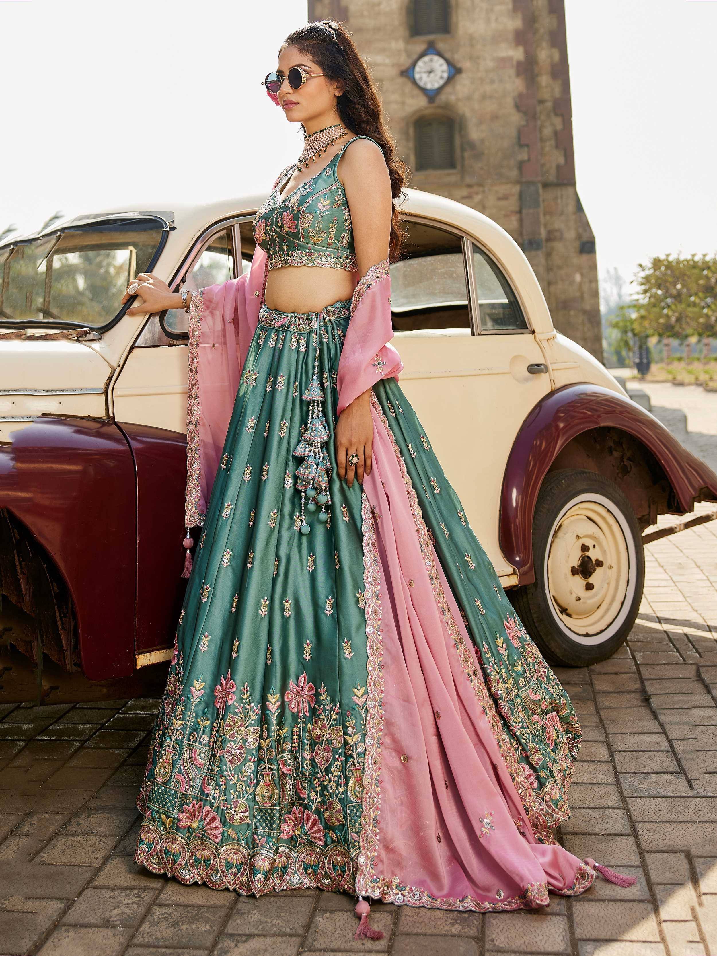 Green and pink embroidered lehenga choli with floral motifs, worn by woman beside vintage car