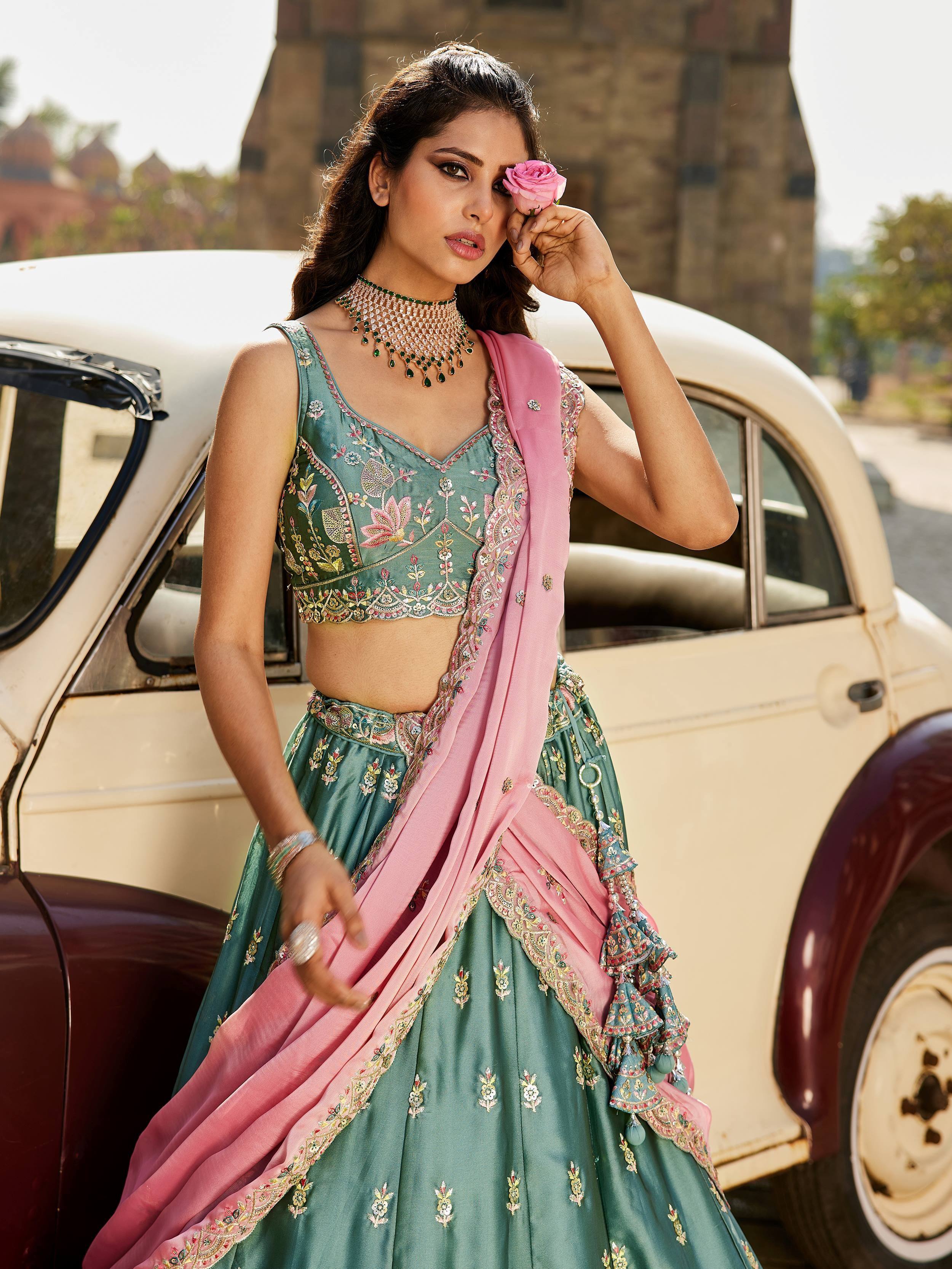 Elegant green embroidered lehenga choli with pink dupatta, styled with jewelry and rose, near vintage car
