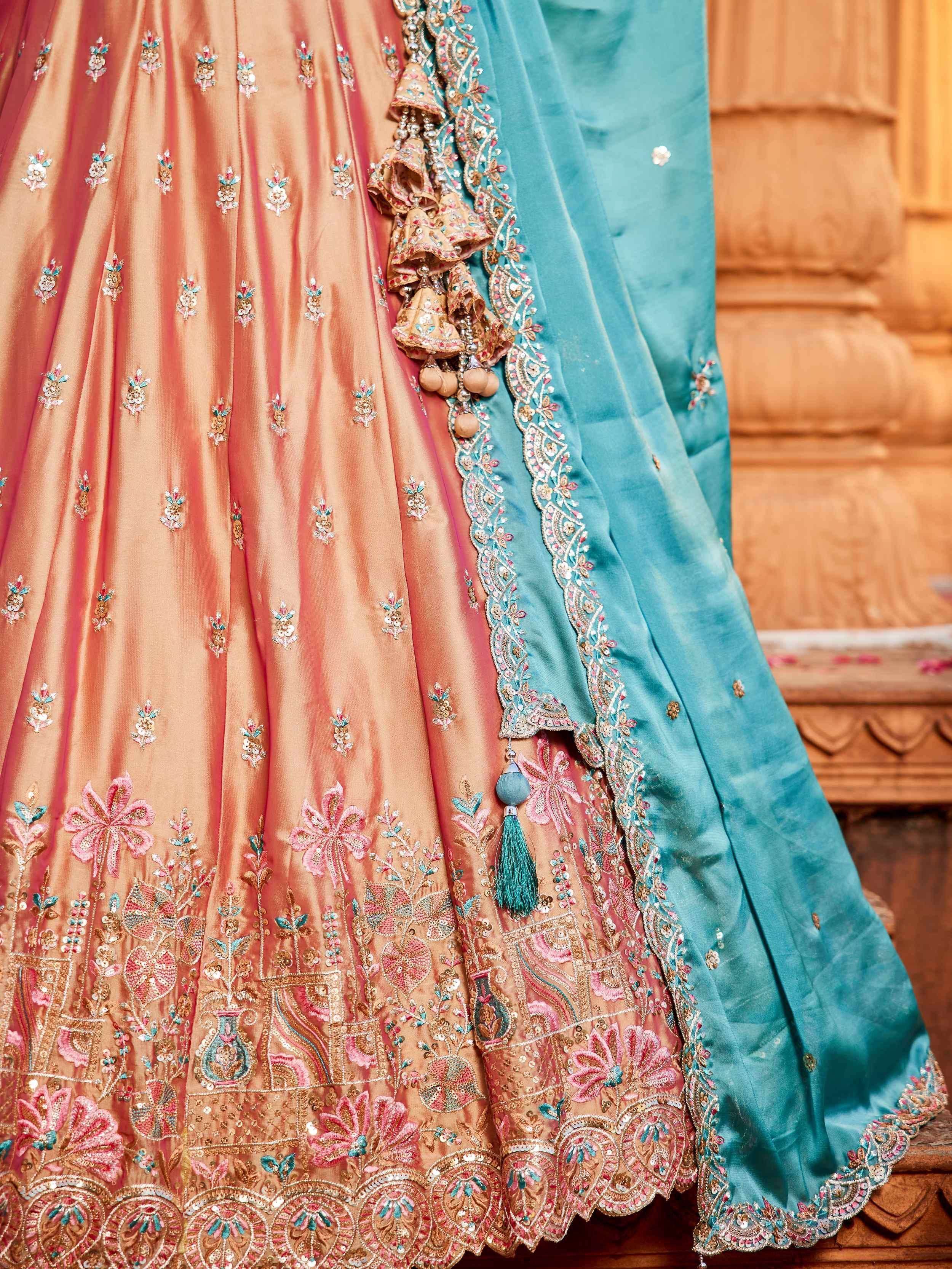 Peach and teal designer lehenga choli with floral embroidery and tassels, perfect for Indian weddings.