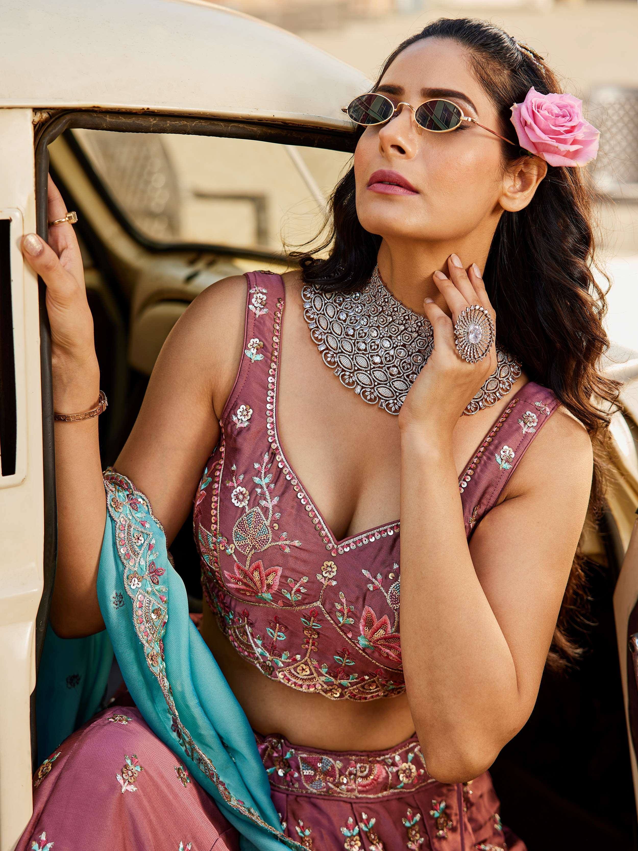 Woman in embroidered maroon lehenga choli with blue dupatta, floral hair accessory, and statement jewelry near vintage car