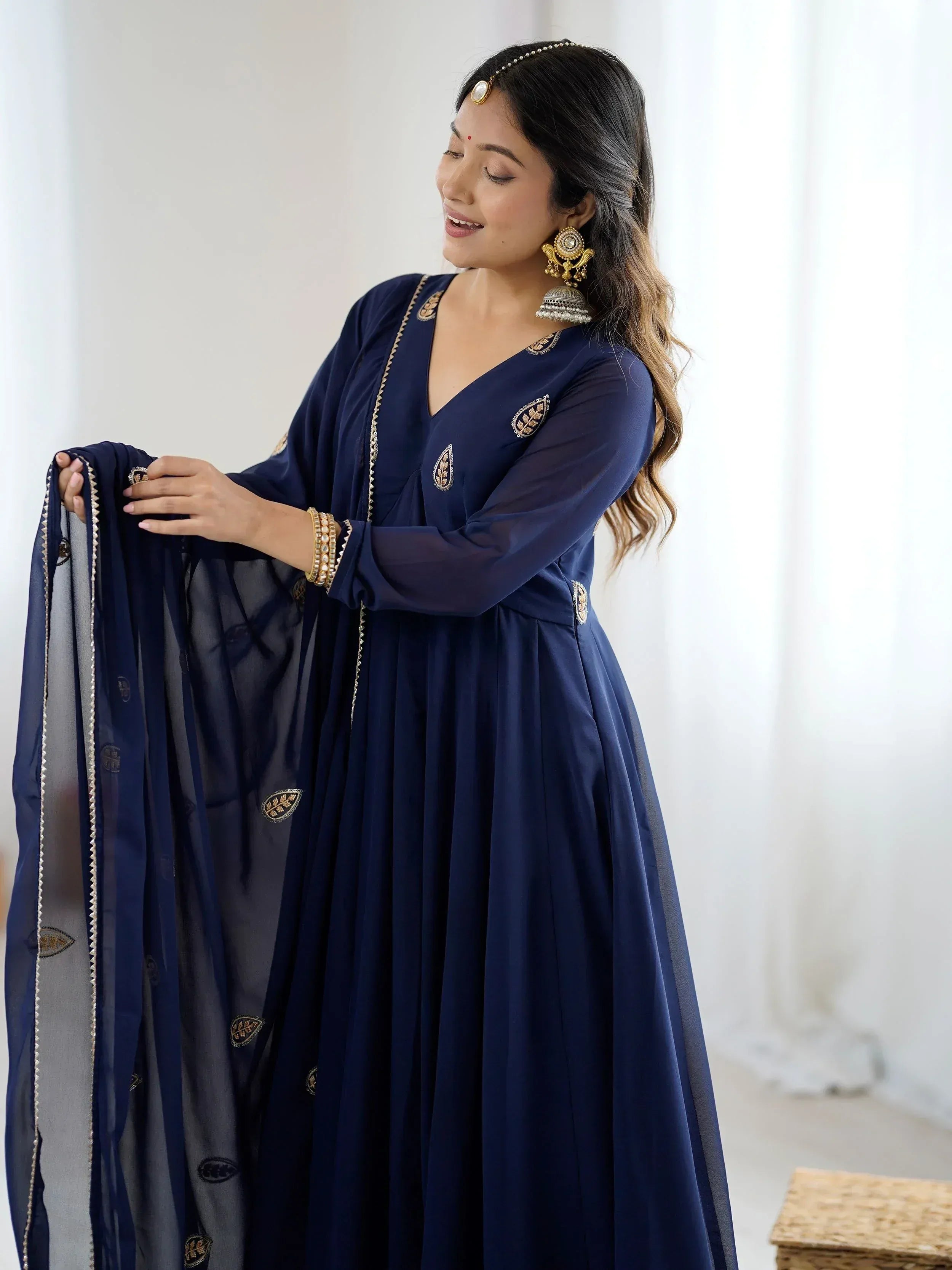 Navy blue ethnic gown with gold embroidery, paired with matching dupatta and traditional jewelry for festive occasions.