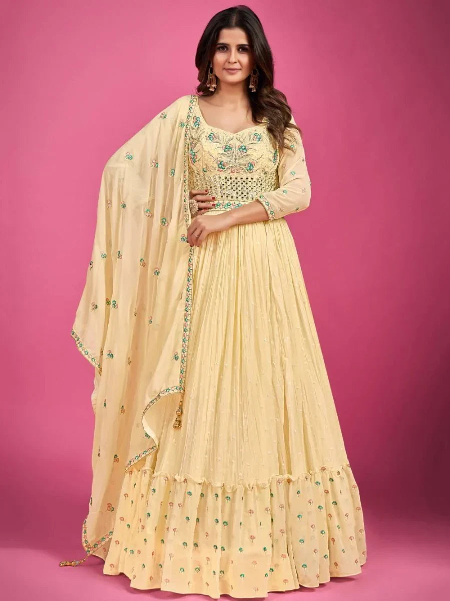 Woman wearing light yellow embroidered ethnic gown with dupatta, pink background