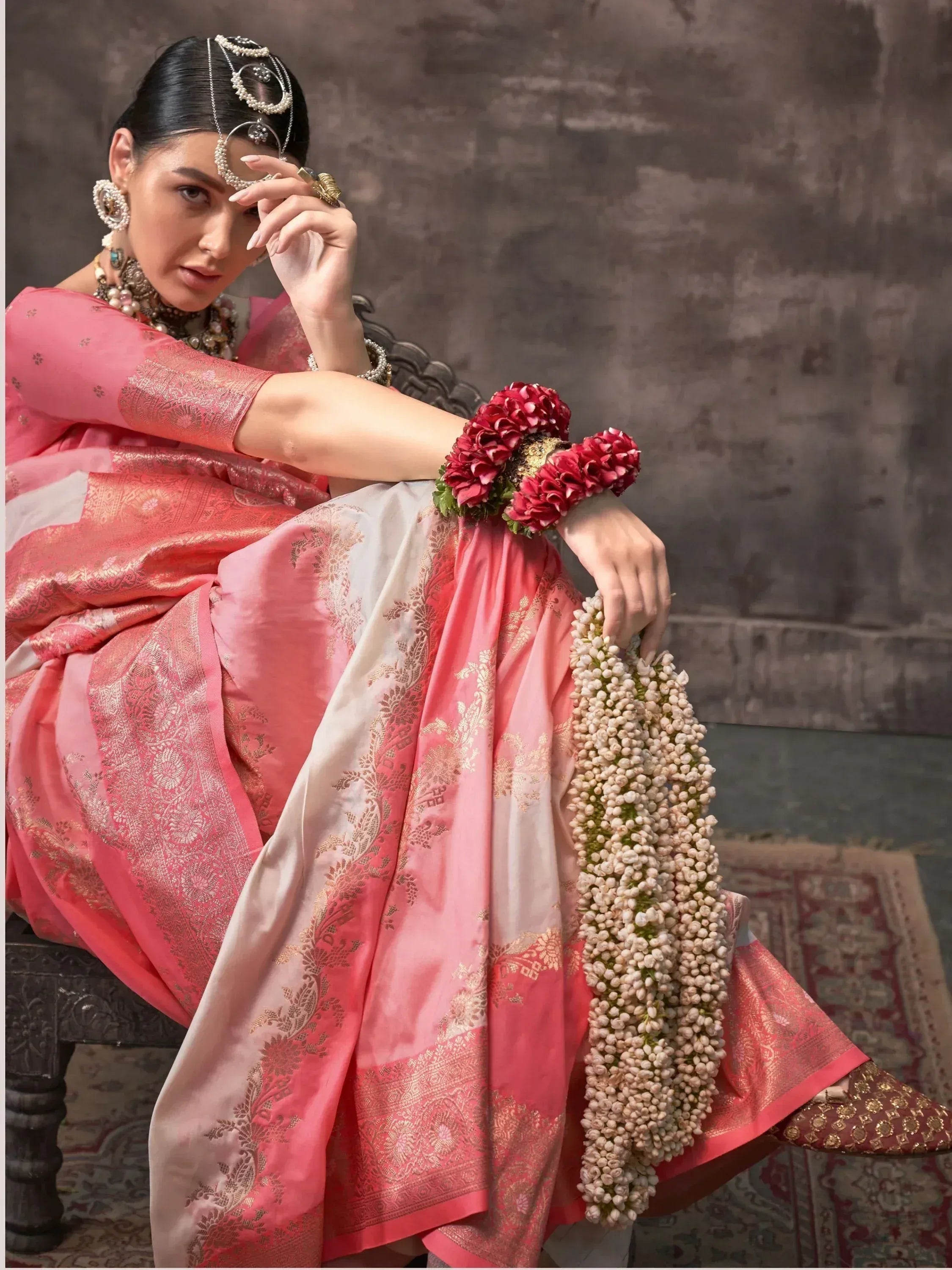 Woman in pink and white designer saree with gold embroidery, floral jewelry, and traditional Indian accessories