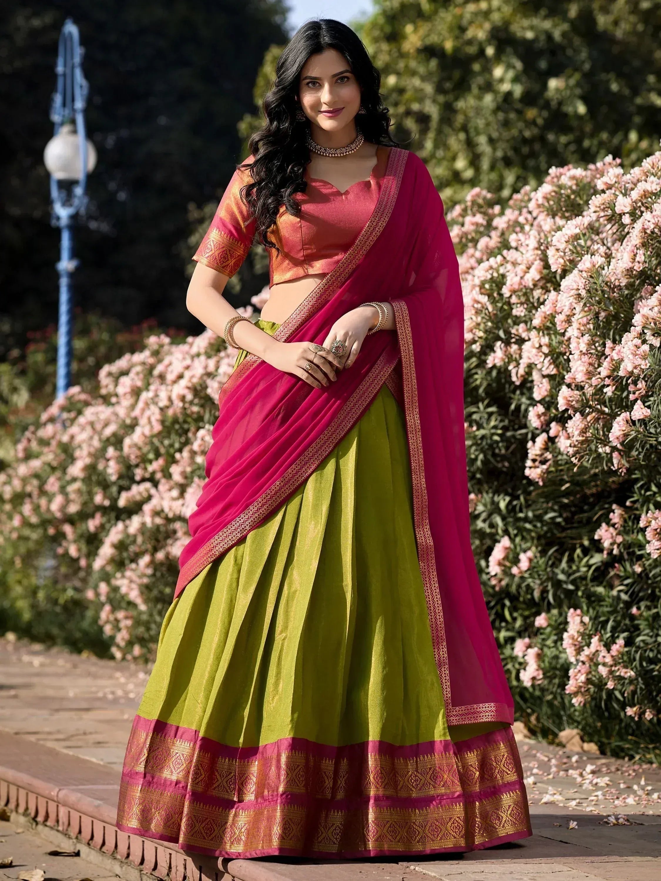 Woman in vibrant green and pink lehenga choli with golden border, perfect for Indian ethnic occasions