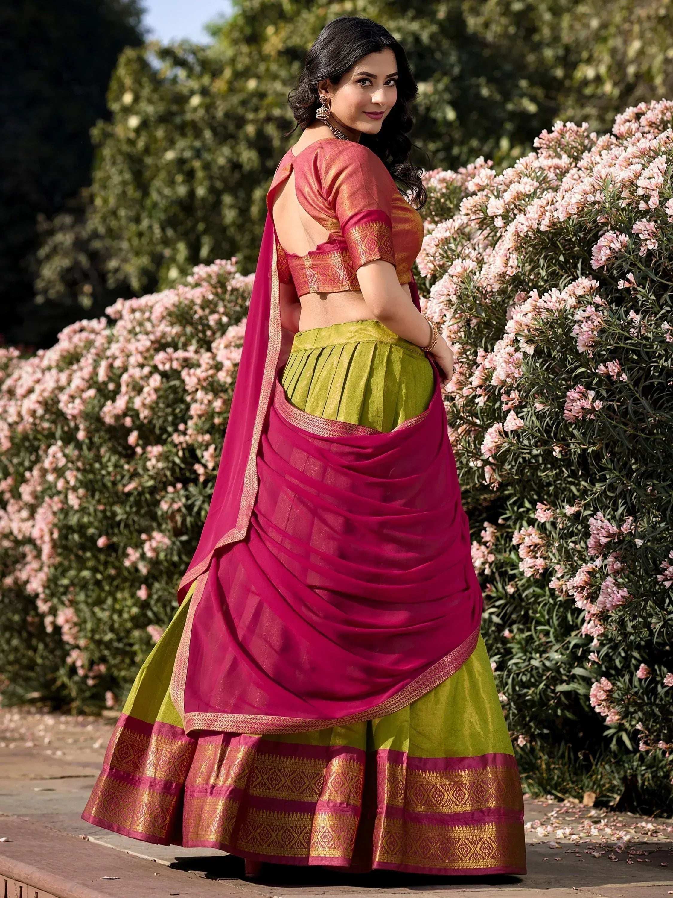 Woman in vibrant pink and green designer lehenga choli with gold border, perfect for Indian ethnic occasions