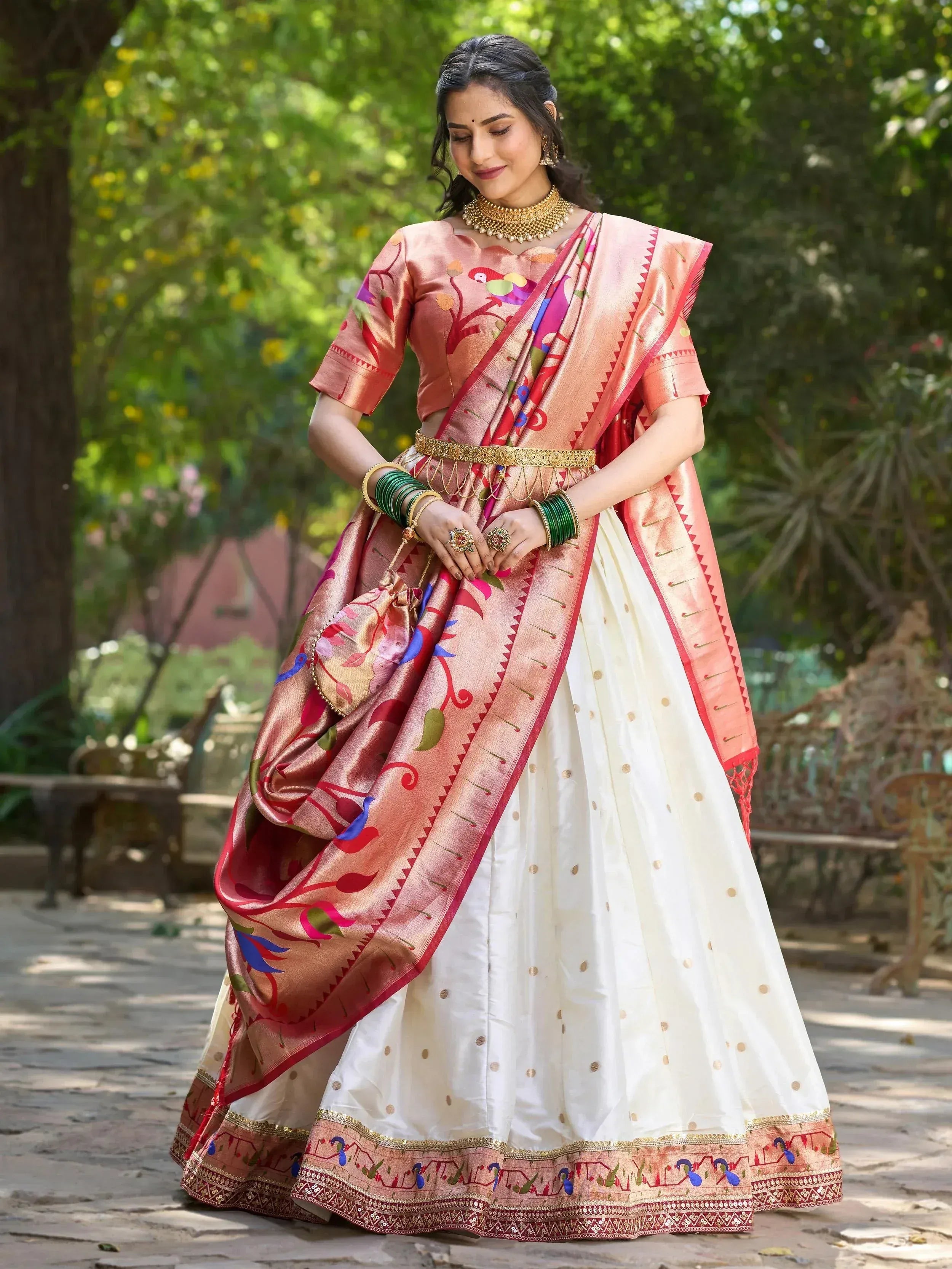 Woman in elegant Indian lehenga choli with colorful bird print, gold jewelry, and floral garden backdrop