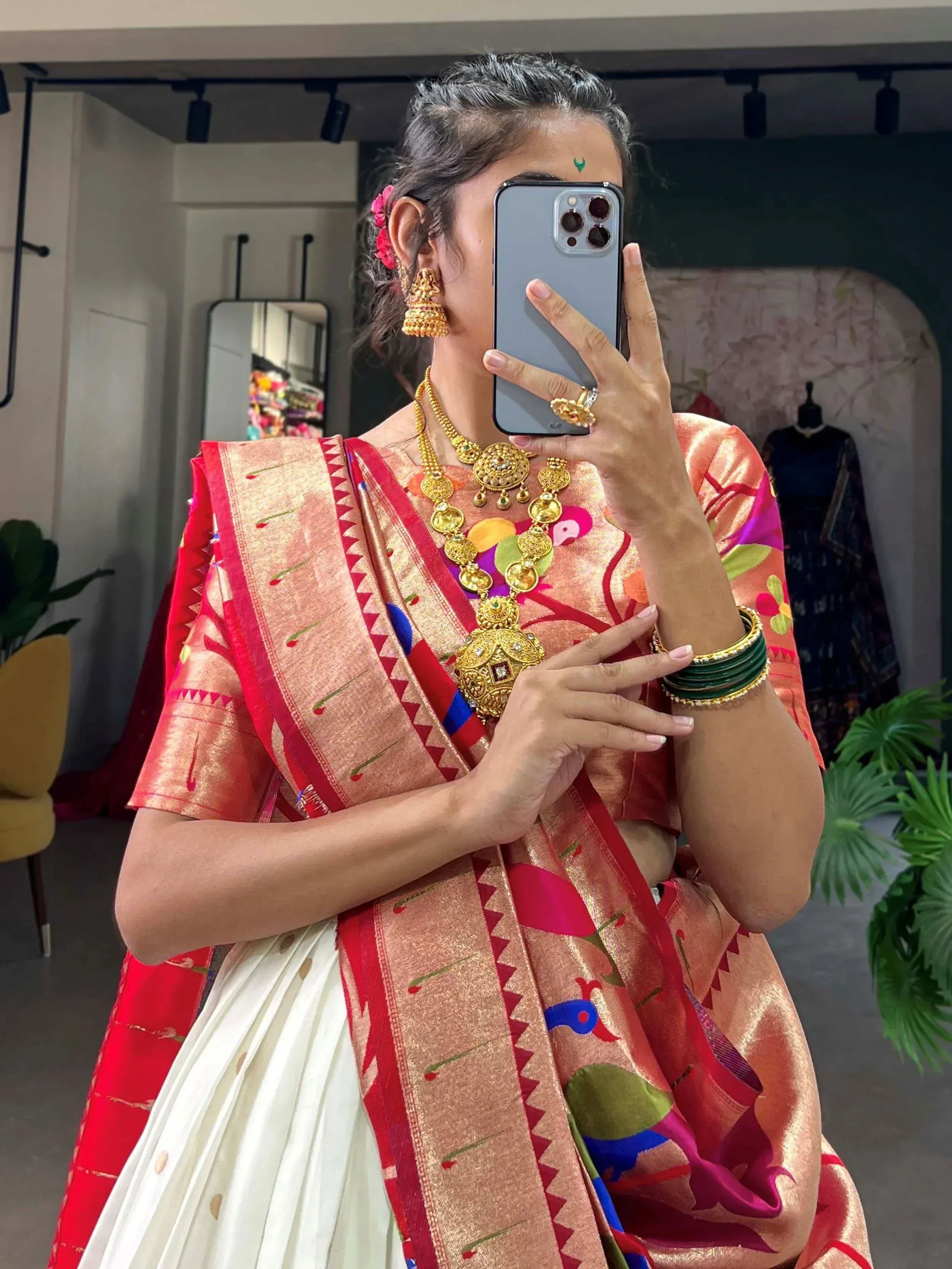 Woman in vibrant Indian saree with gold jewelry, taking mirror selfie in boutique