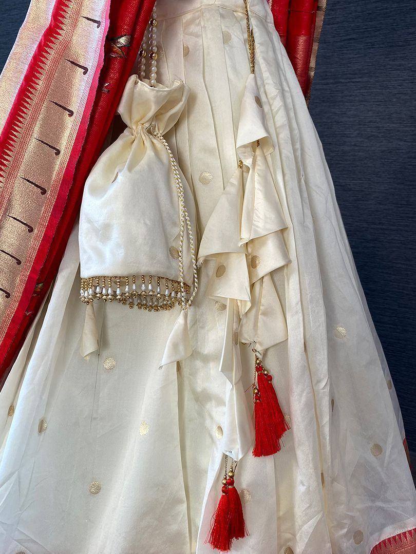 Cream lehenga with gold polka dots, red tassels, and matching potli bag for Indian ethnic wear