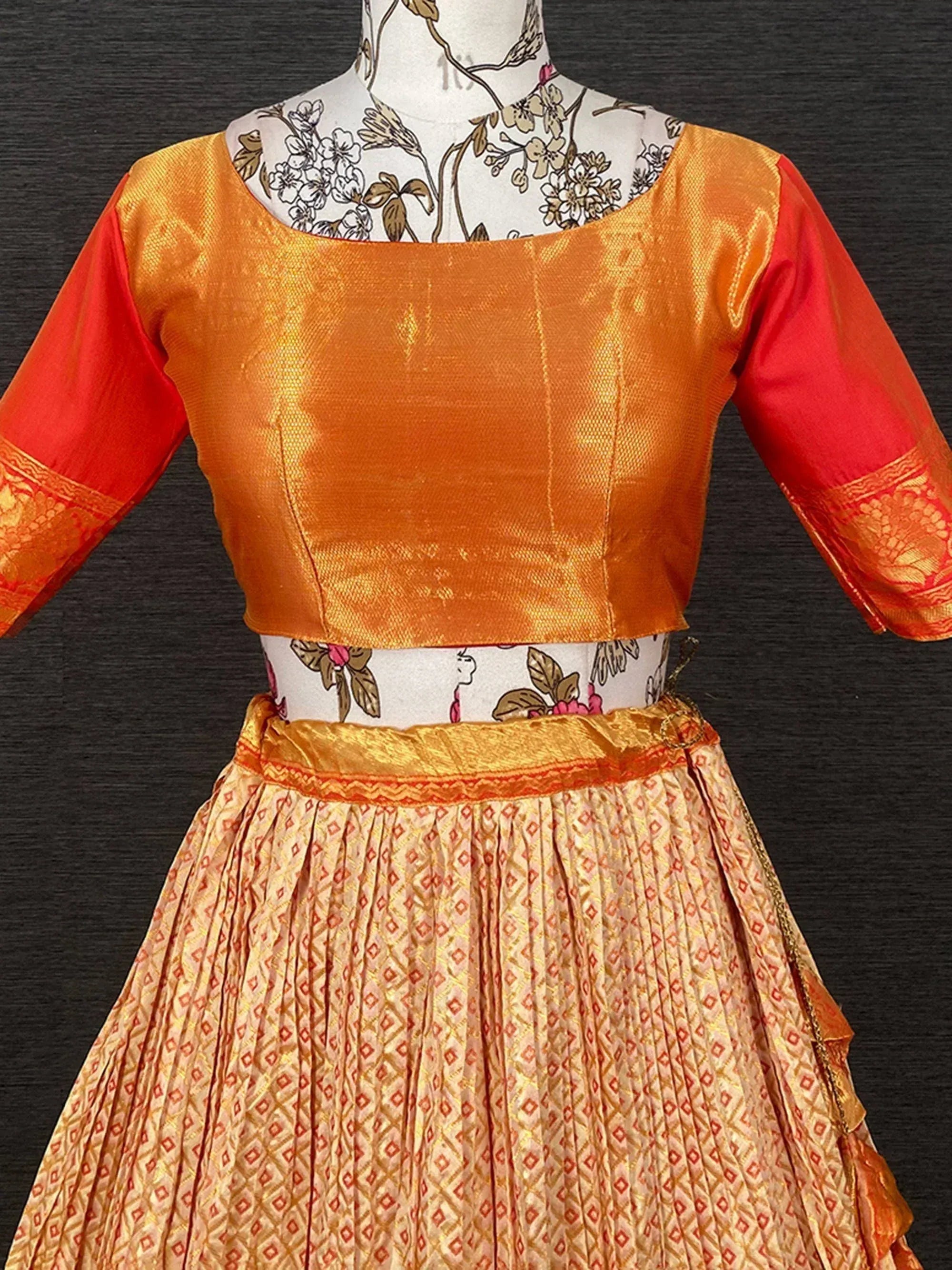 Orange and red ethnic lehenga choli with gold embroidery and pleated skirt, perfect for festive occasions.
