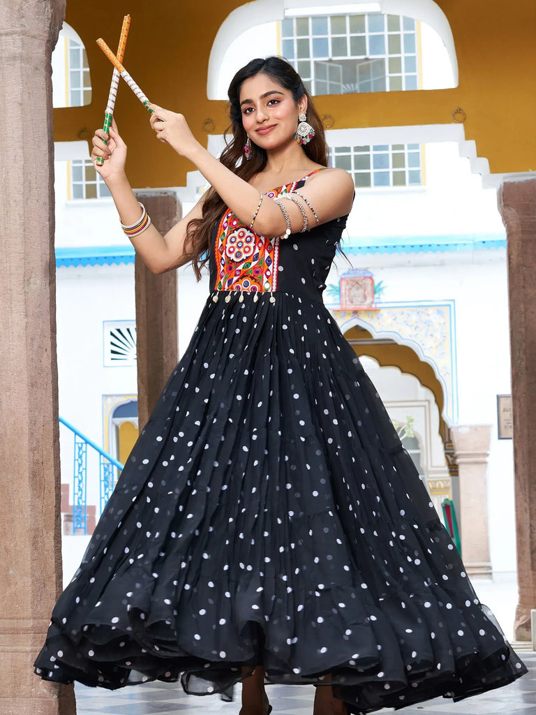 Woman in black polka dot ethnic gown with colorful embroidery, holding dandiya sticks, traditional Indian attire