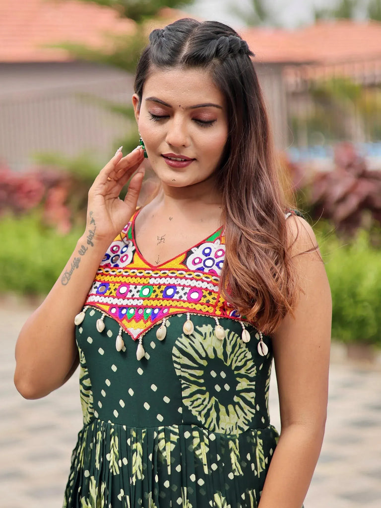 Woman in green ethnic gown with colorful mirror work and shell tassels, perfect for Indian festive wear.