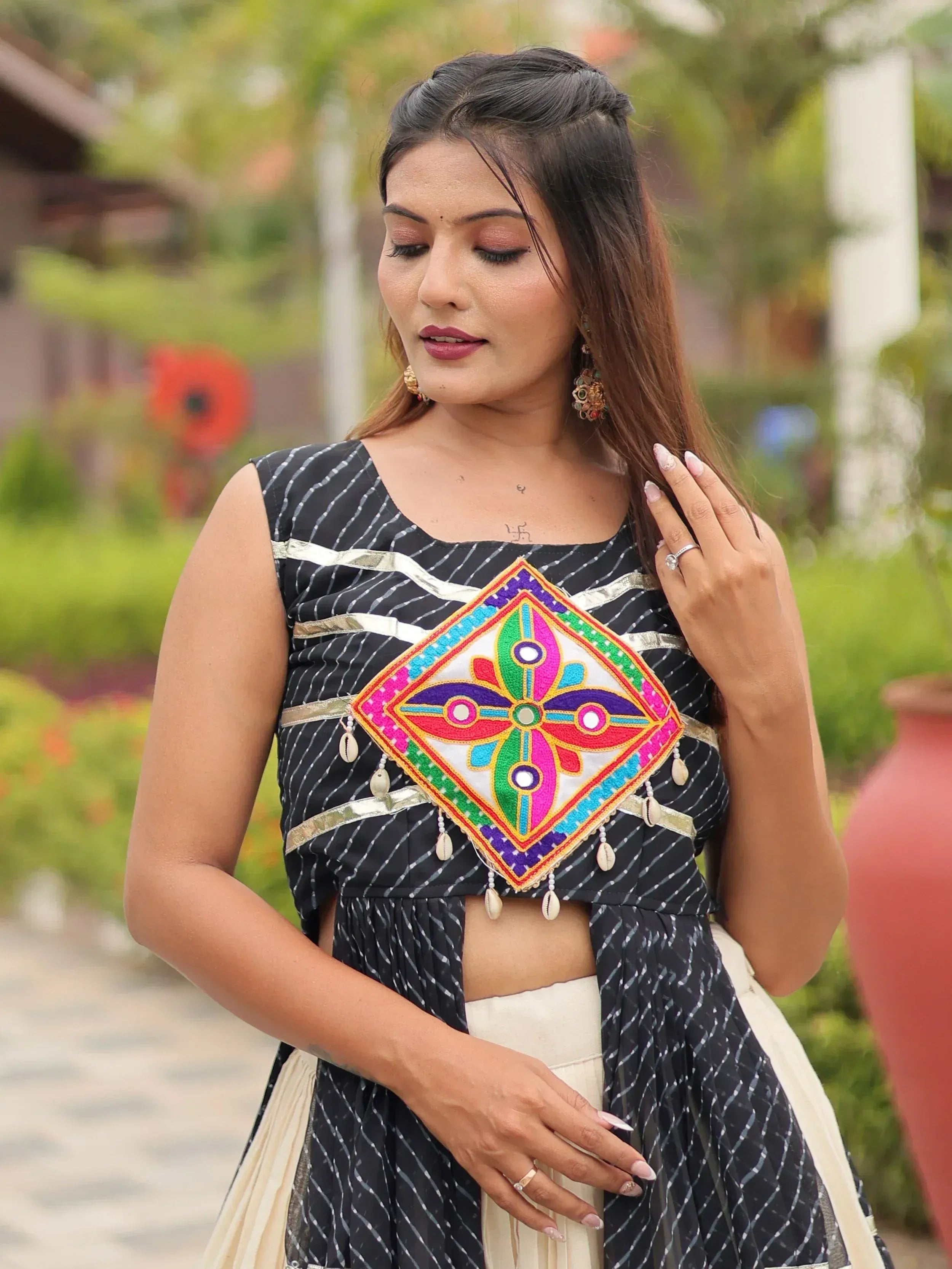 Woman in black and white striped ethnic top with colorful mirror work and shell embellishments, paired with cream skirt