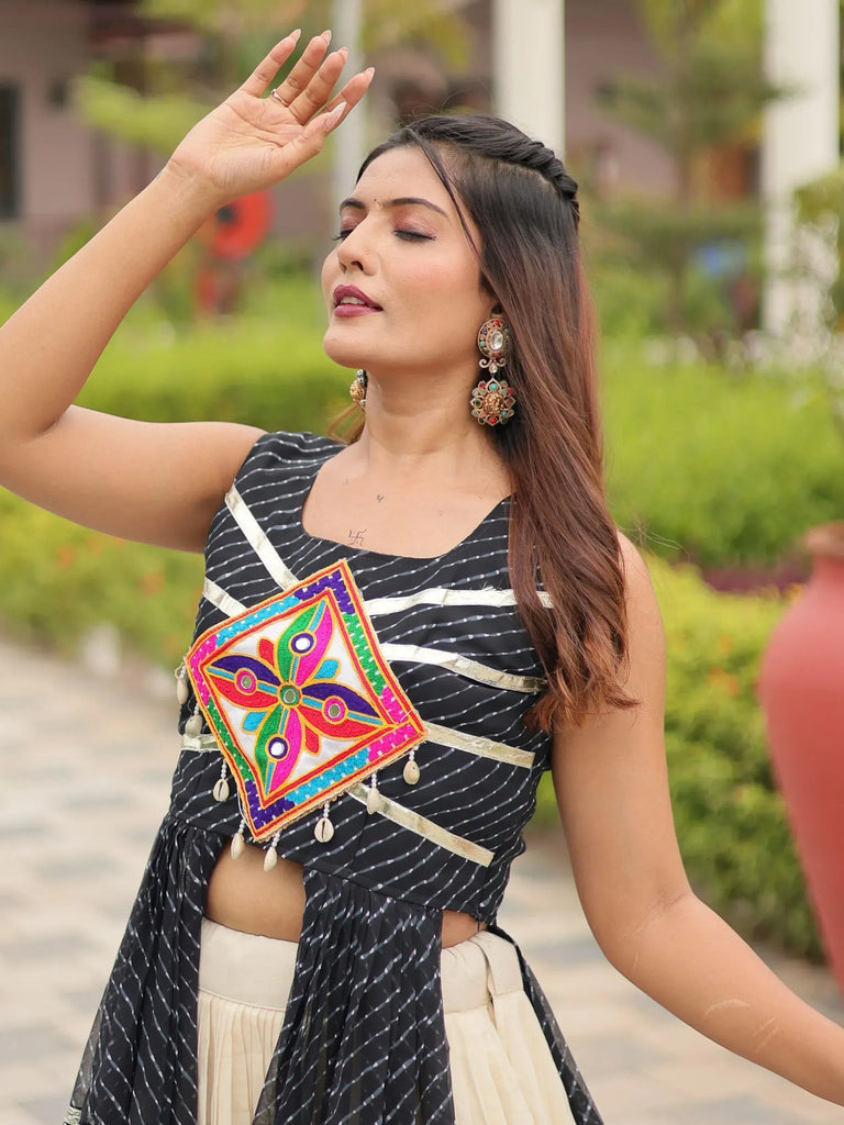 Woman in black and white striped ethnic top with colorful embroidered patch and shell tassels, paired with cream skirt, wearing statement earrings.