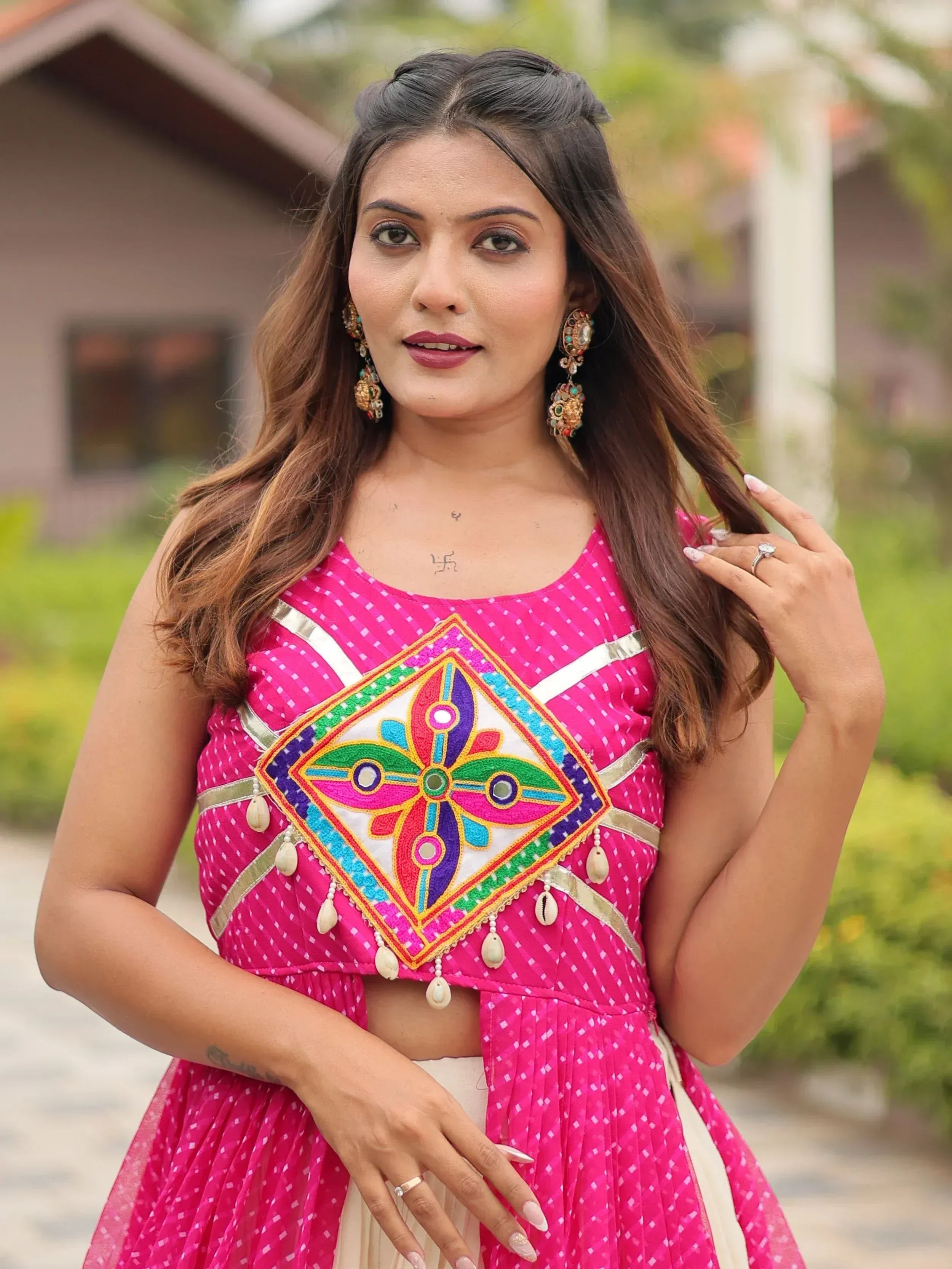 Woman in vibrant pink ethnic wear with mirror work and shell embellishments, perfect for Indian festivities.