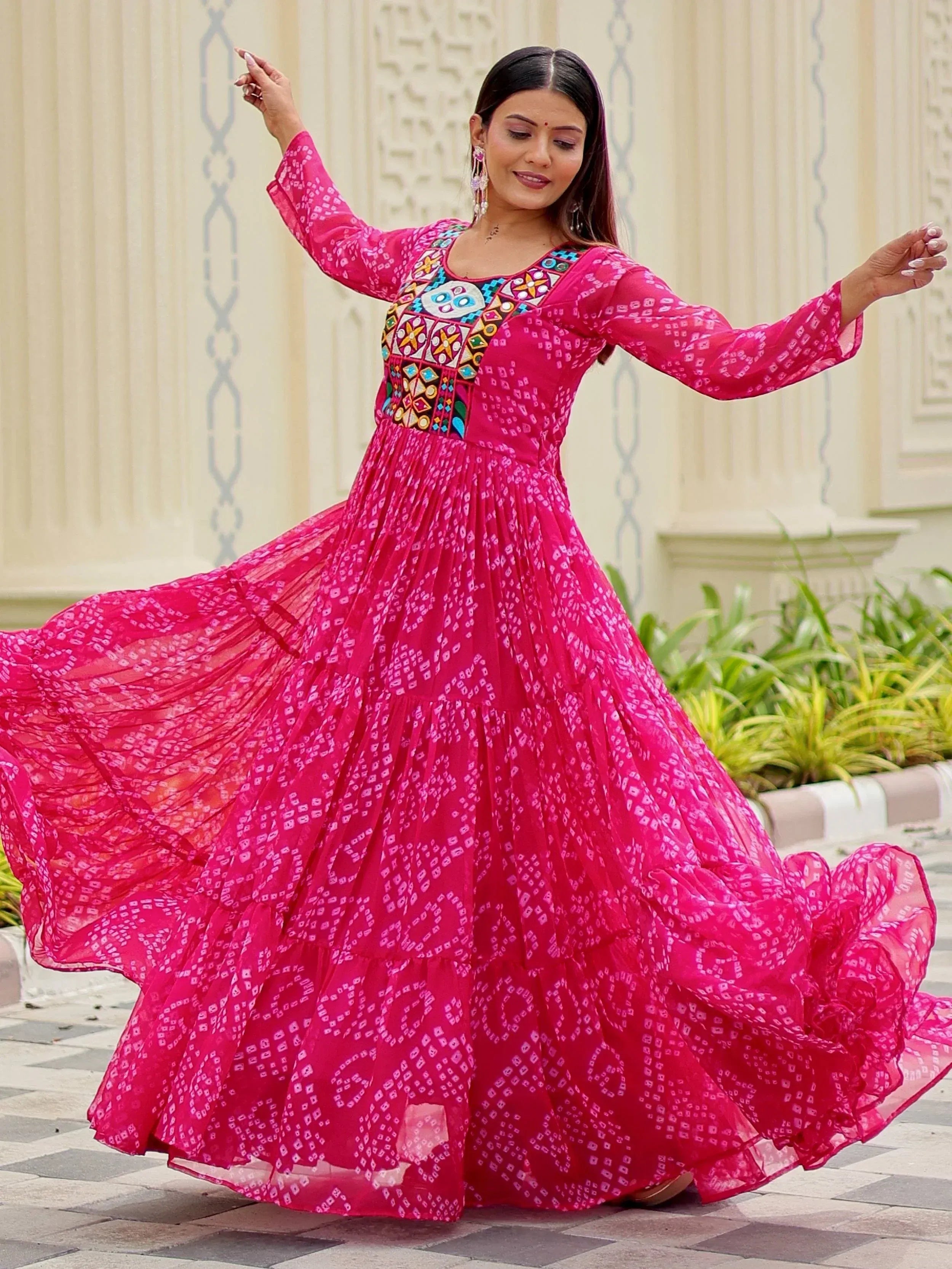 Woman twirling in vibrant pink ethnic gown with colorful embroidery and bandhani print, perfect for Indian festive wear.