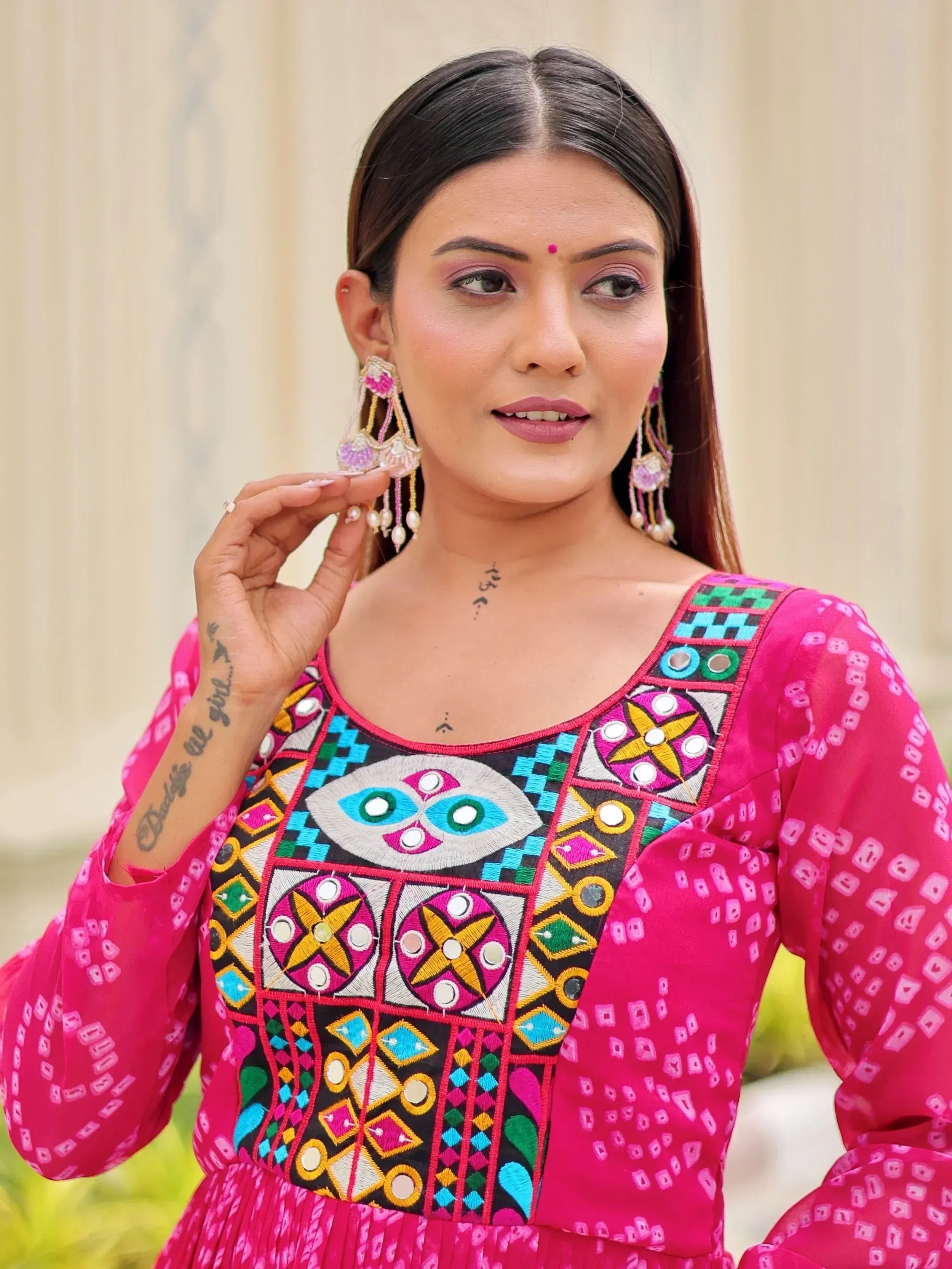 Woman in vibrant pink ethnic dress with colorful mirror embroidery and traditional earrings