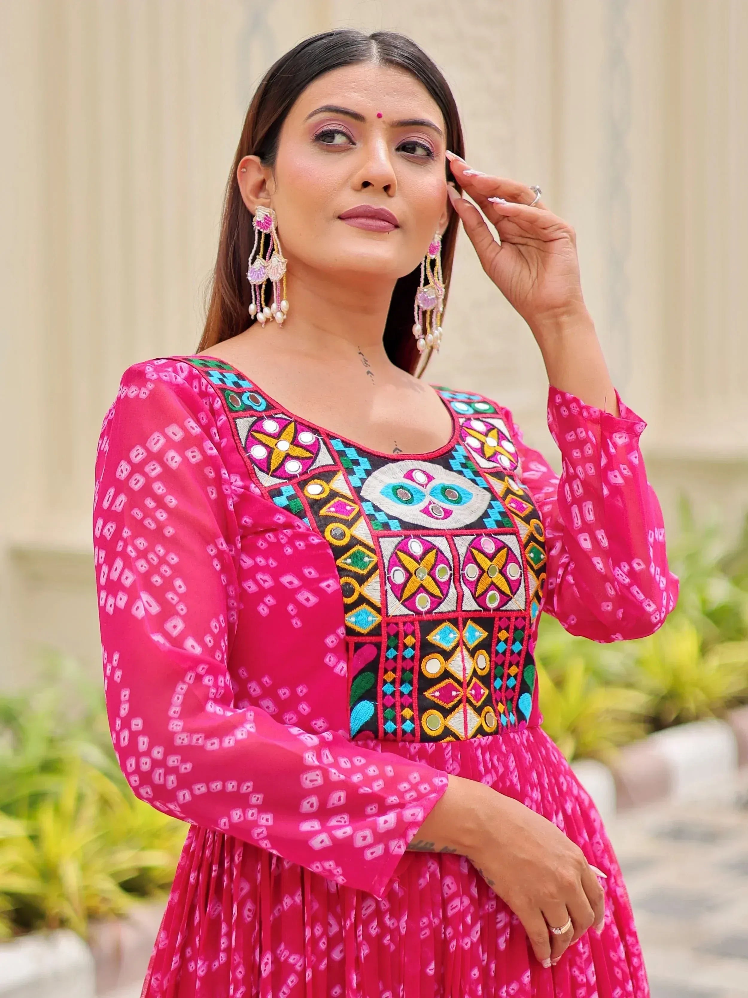 Woman in vibrant pink ethnic gown with colorful mirror embroidery and statement earrings