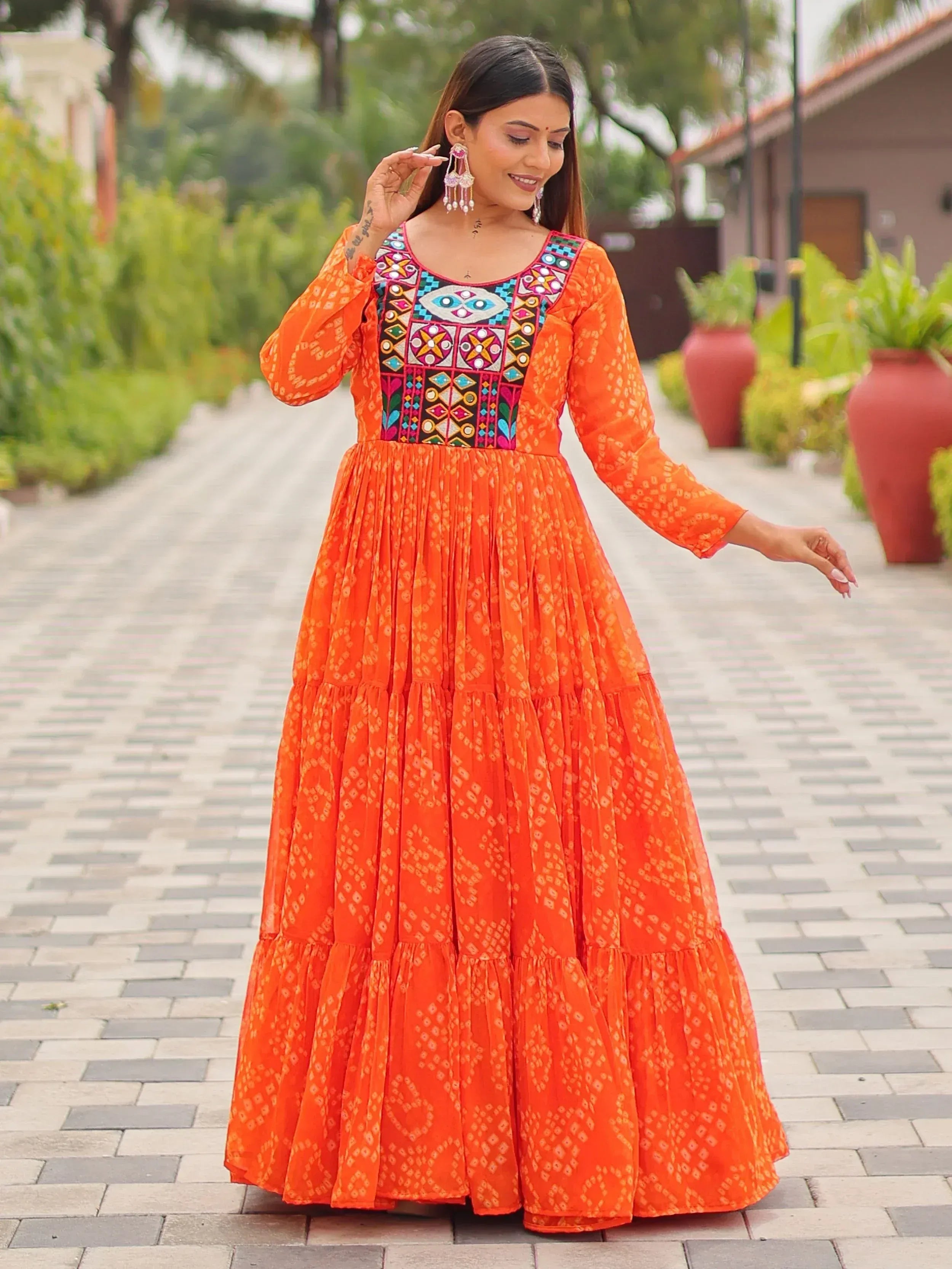 Orange ethnic gown with colorful embroidery and tiered skirt, perfect for Indian festive wear