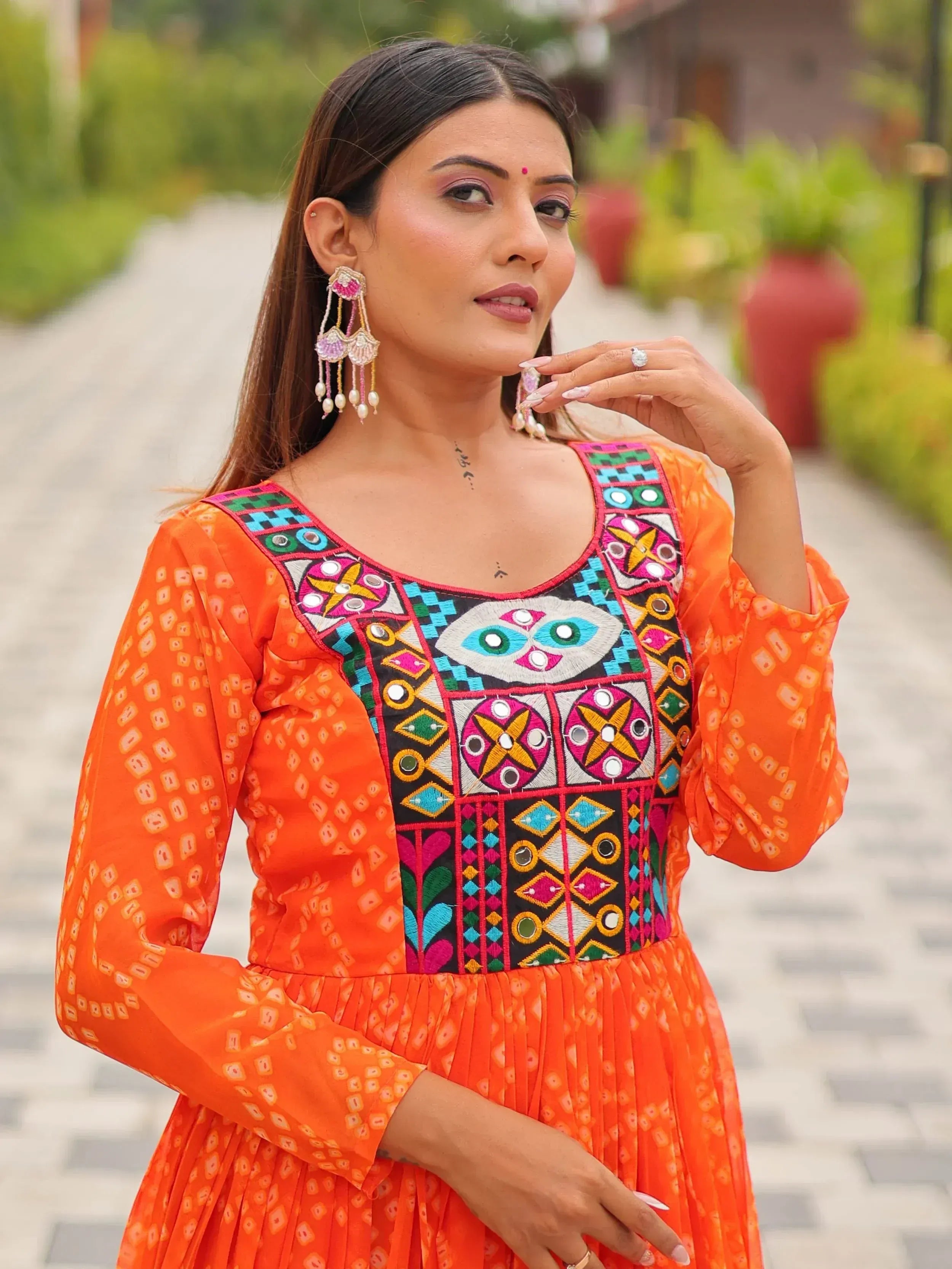 Orange ethnic gown with mirror work and embroidery, styled with statement earrings for festive occasions