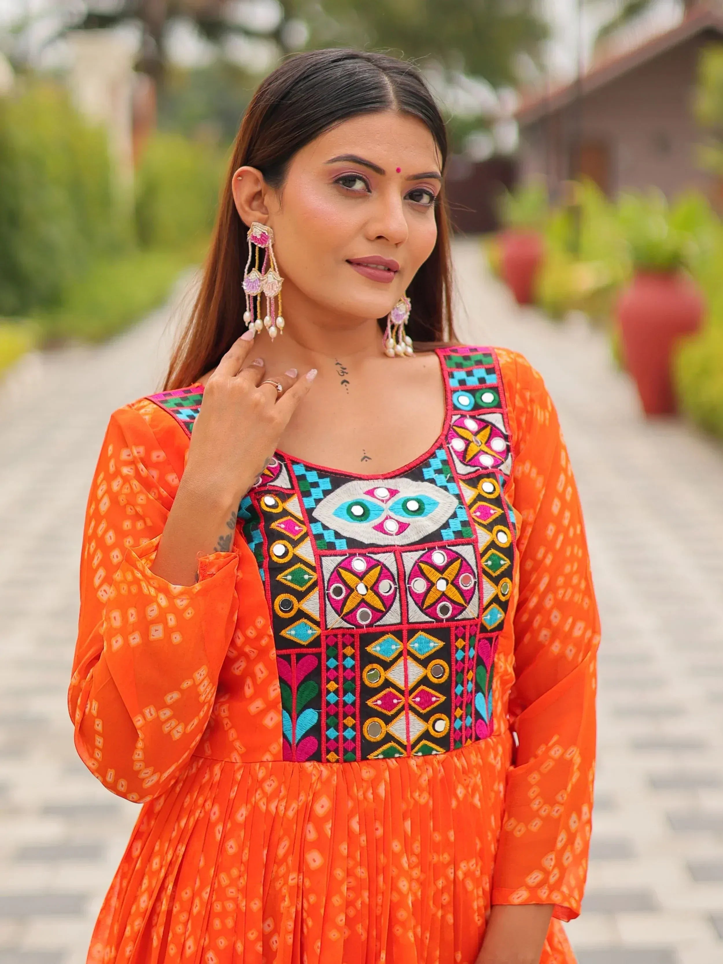 Vibrant orange ethnic gown with colorful mirror embroidery and bell sleeves, perfect for festive occasions.