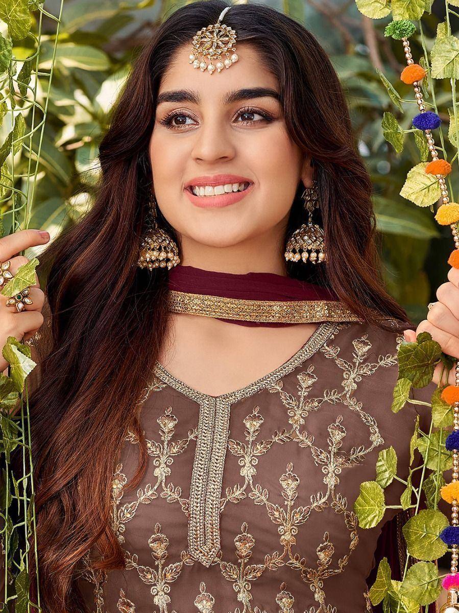 Woman in brown embroidered ethnic suit with gold jewelry and dupatta outdoors