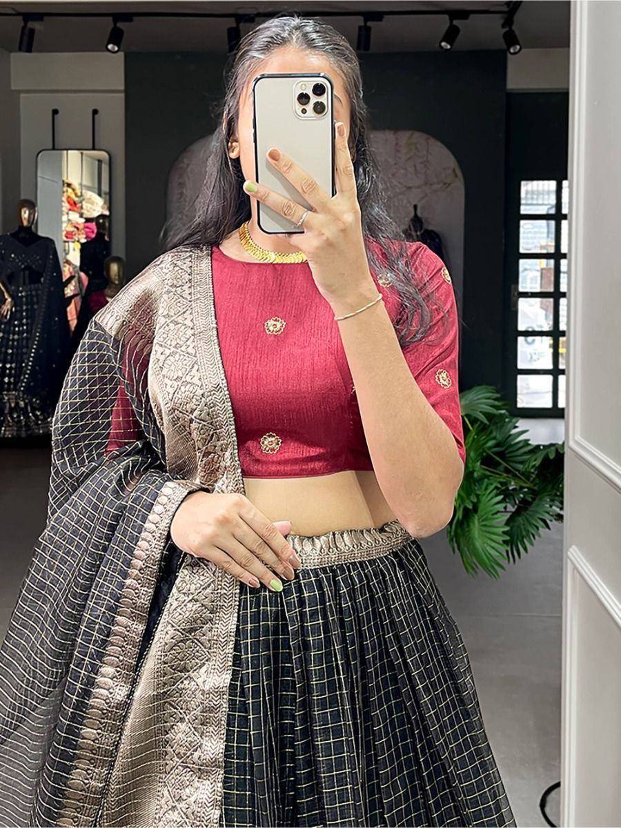 Woman in red embroidered blouse and black checkered lehenga with gold dupatta, taking mirror selfie in boutique