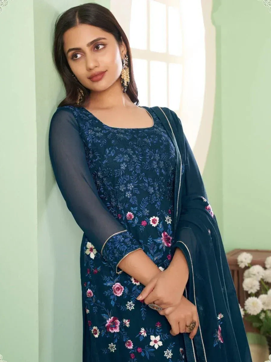 Woman in navy blue floral ethnic gown with sheer sleeves and dupatta, indoor setting