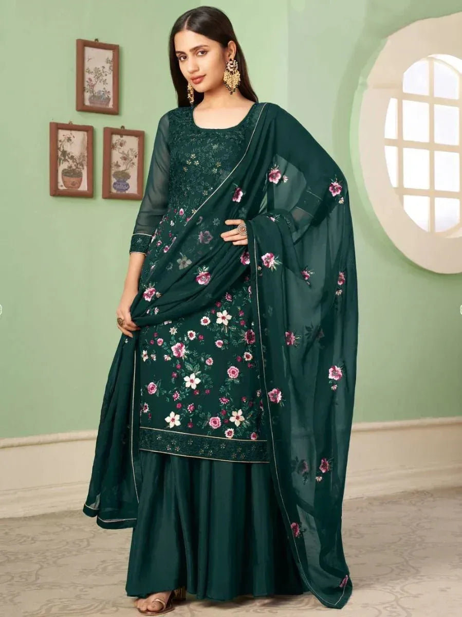 Woman in dark green floral embroidered salwar kameez with dupatta, posing indoors