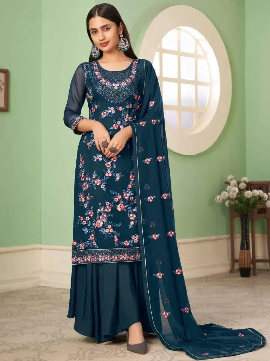 Woman wearing a navy blue floral embroidered salwar kameez with dupatta in a room.