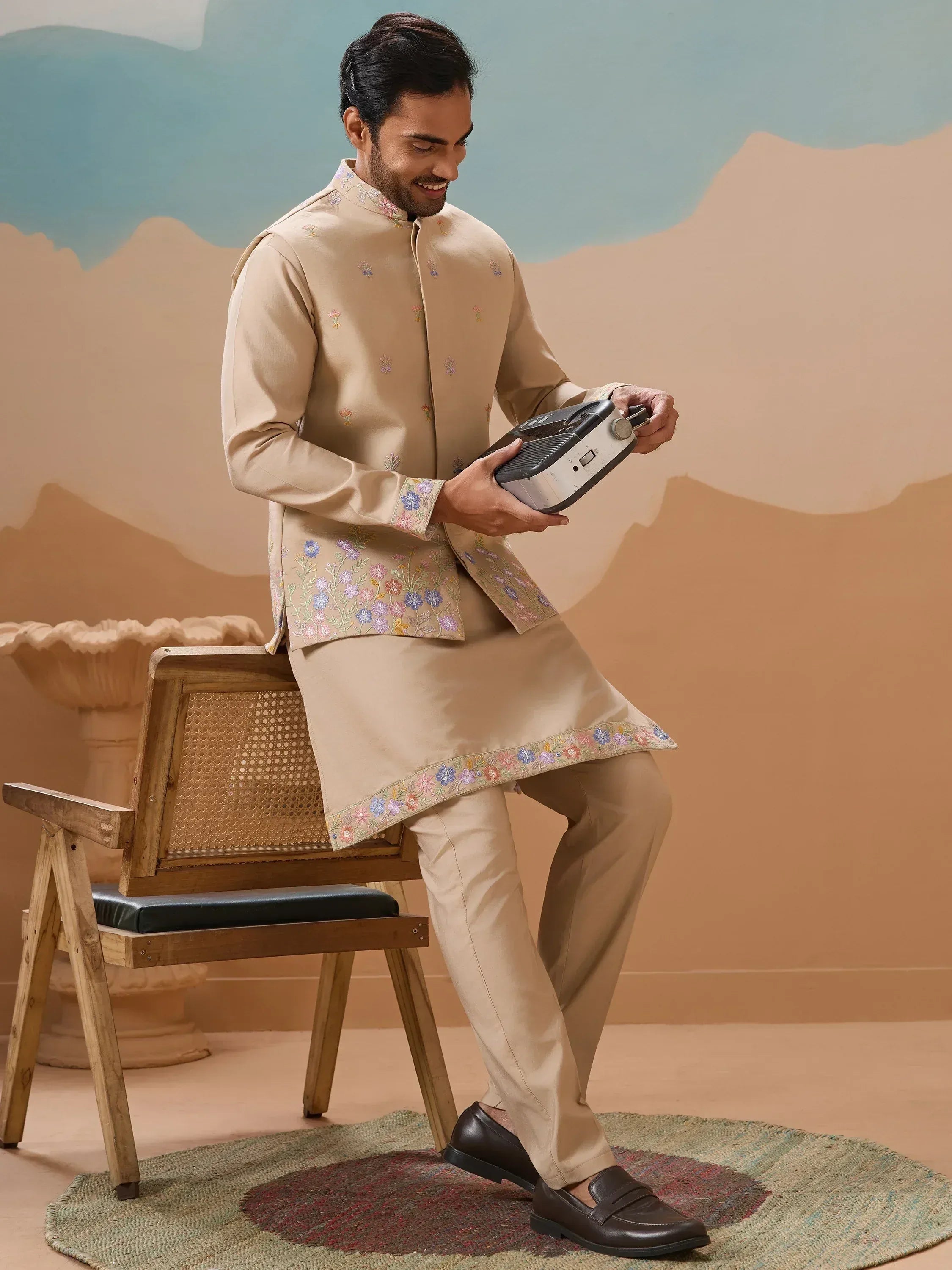 Man in beige embroidered kurta set with floral details, holding vintage radio, styled for Indian ethnic wear