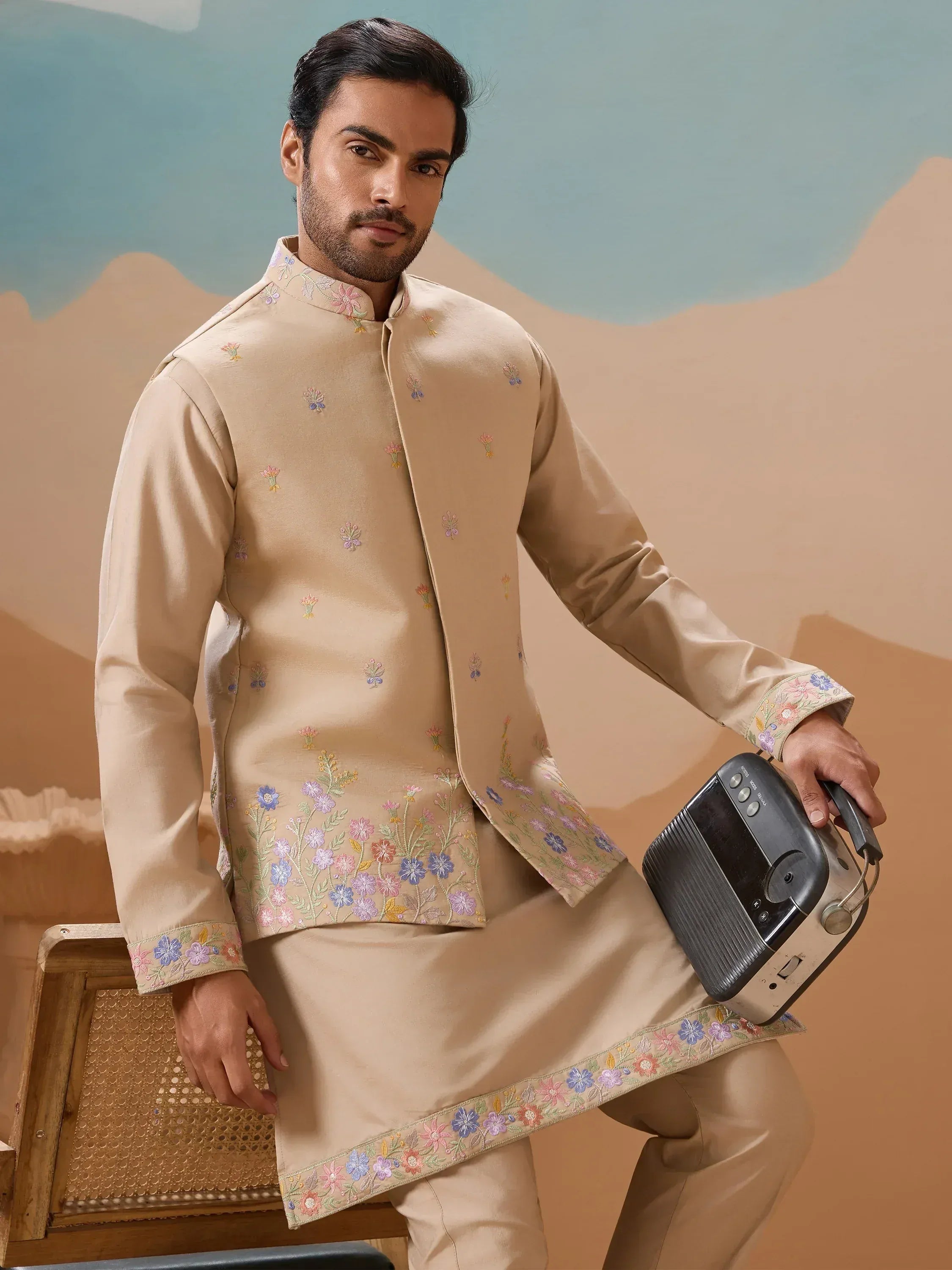 Man in beige embroidered kurta set with floral details, holding vintage radio, perfect for Indian ethnic wear occasions