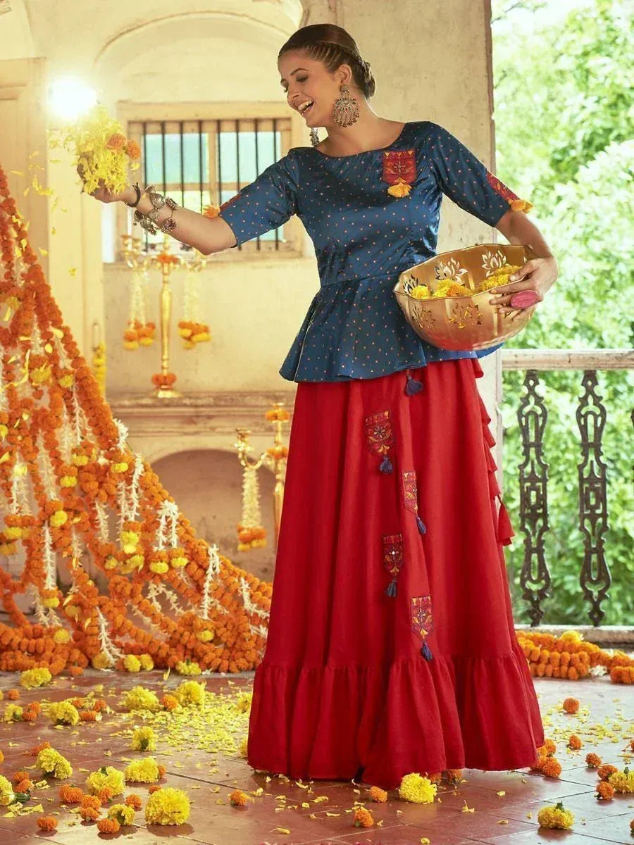 Woman in blue peplum top and red embroidered skirt, celebrating with marigold flowers, Indian ethnic wear