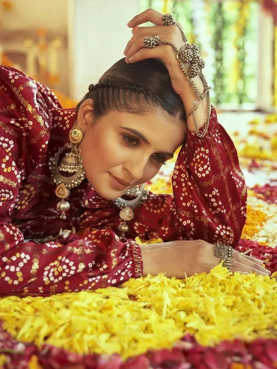 Woman in maroon ethnic salwar kameez with gold print, traditional jewelry, lying on flower petals