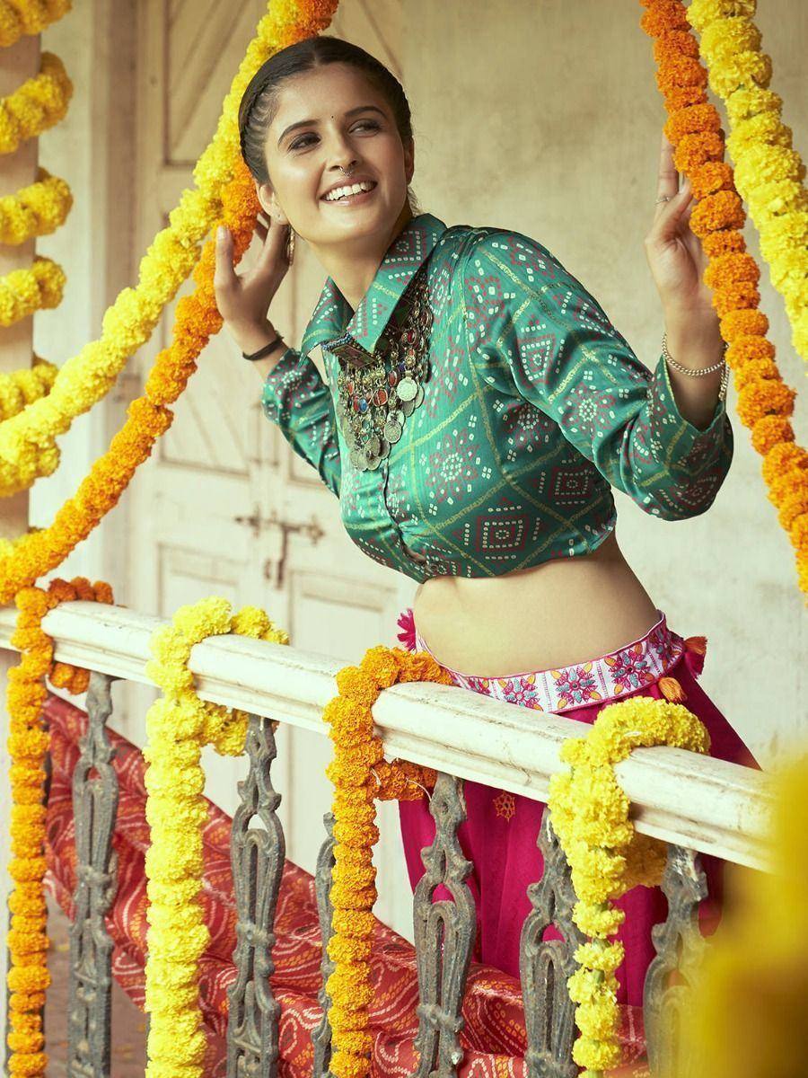 Woman in green printed crop top and pink lehenga, adorned with marigold garlands, perfect for ethnic occasions.