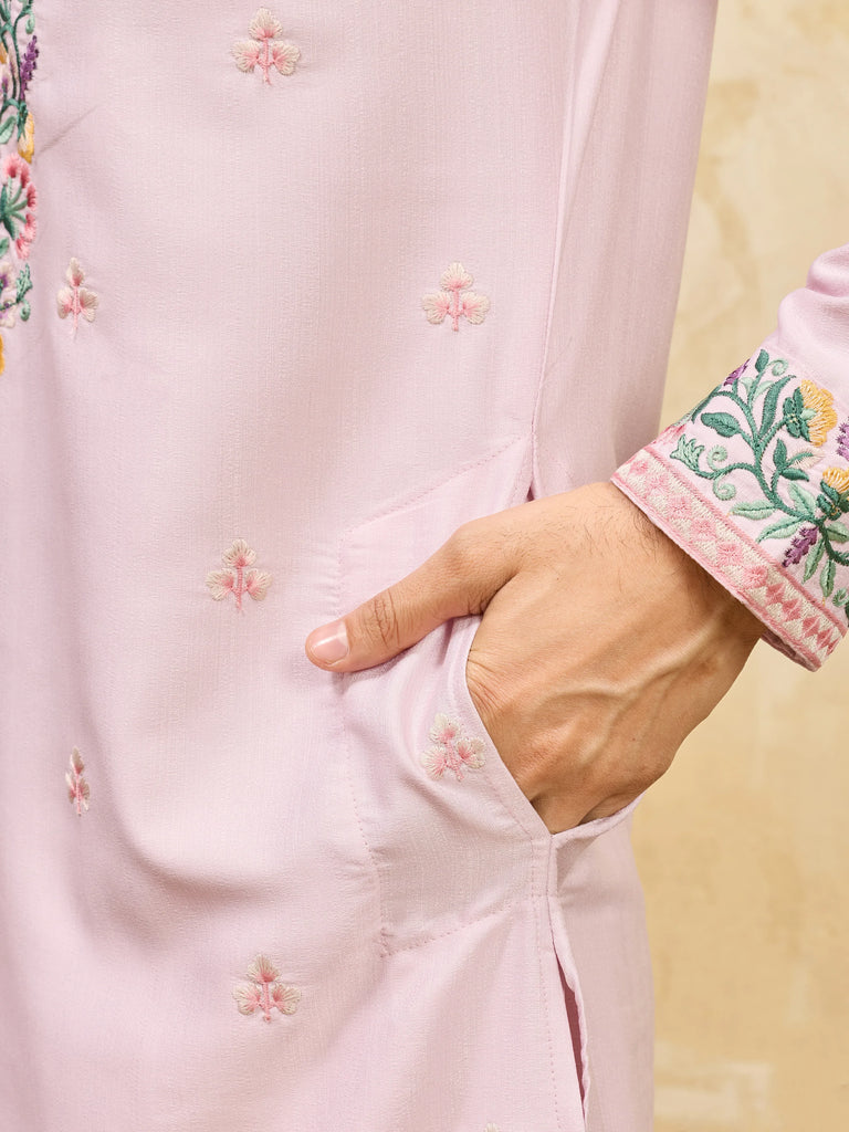 Close-up of a man wearing a light pink embroidered ethnic kurta with a hand in pocket.