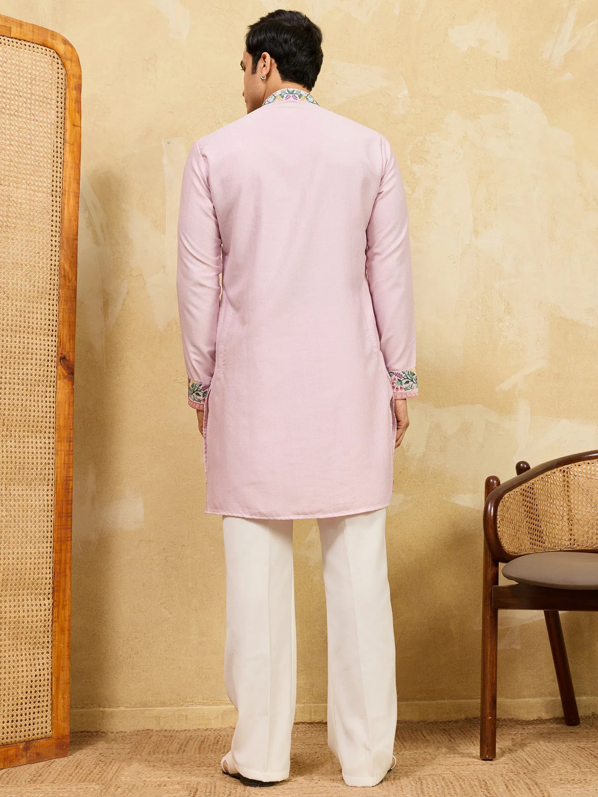Back view of a man wearing a light pink embroidered kurta and white trousers.