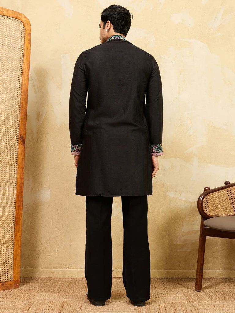 Back view of a man wearing a black ethnic kurta with embroidered cuffs and matching trousers