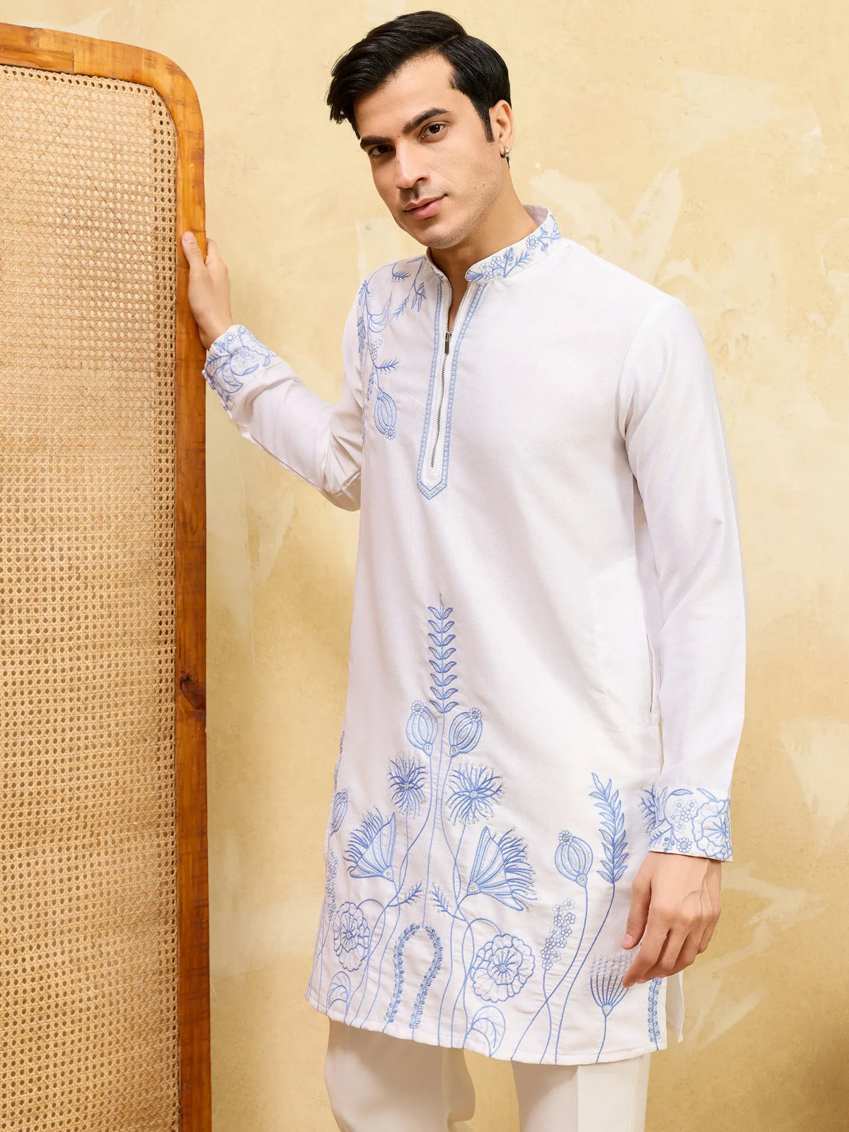 Man wearing a white ethnic kurta with blue floral embroidery and matching trousers.