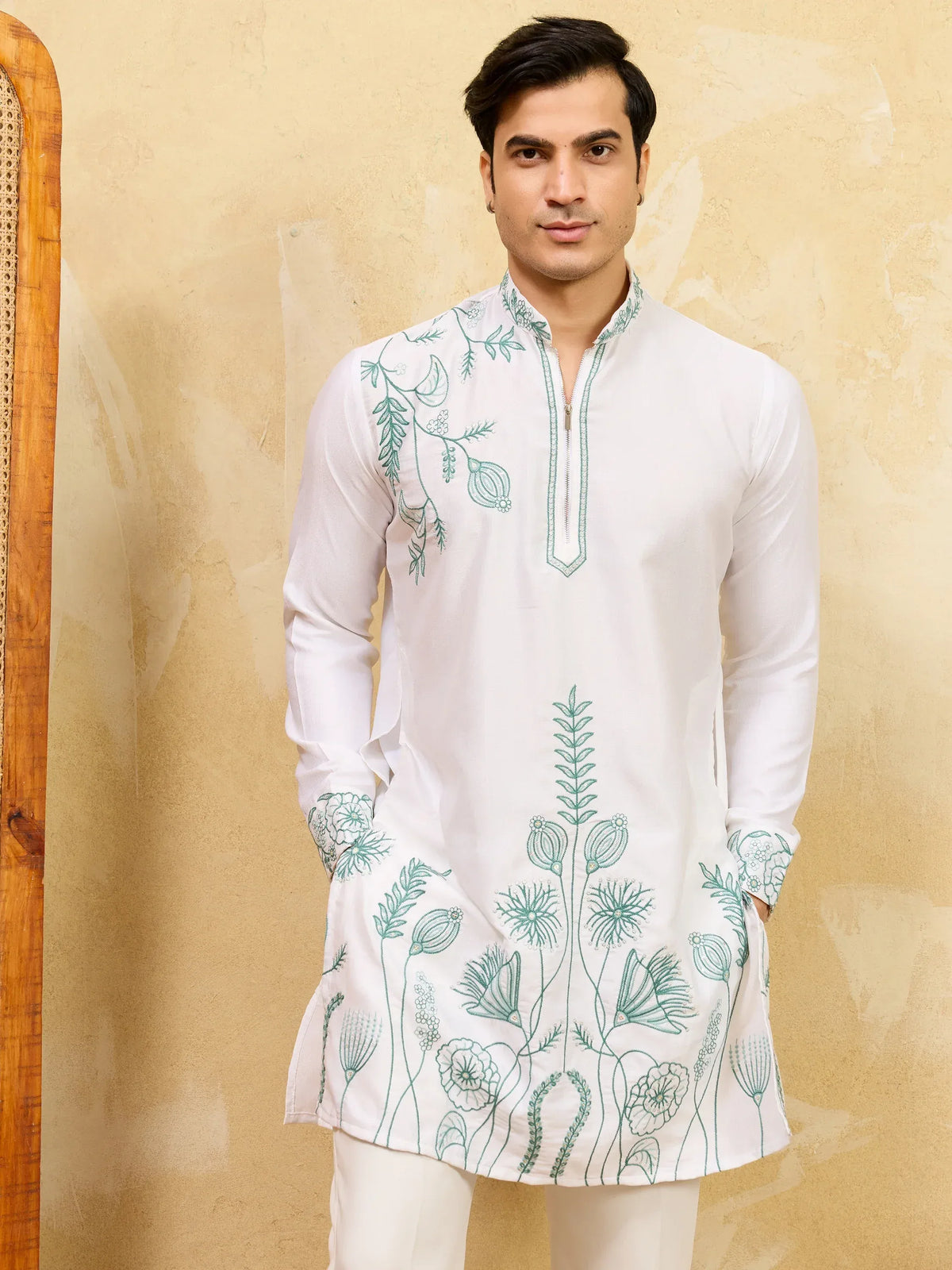 Man wearing a white ethnic kurta with green floral embroidery and matching white trousers.