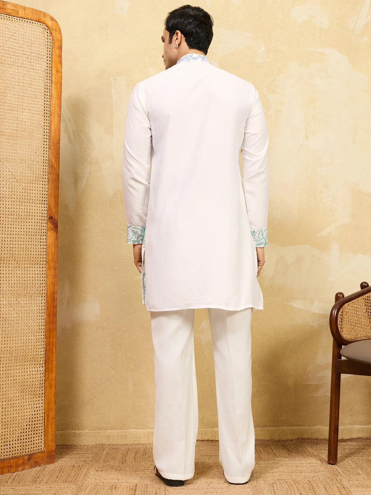 Back view of a man wearing a white ethnic kurta pajama set with blue embroidered cuffs.