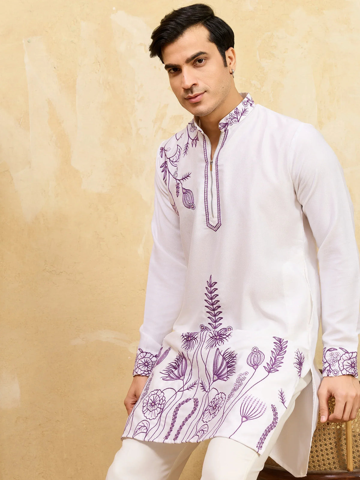 Man wearing a white ethnic kurta with purple floral embroidery on the neck and hem.