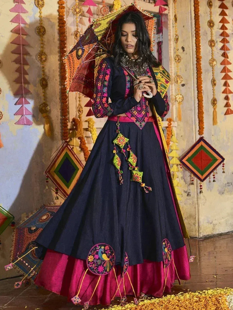 Woman in embroidered navy lehenga choli with pink border, holding decorative umbrella, festive Indian ethnic wear