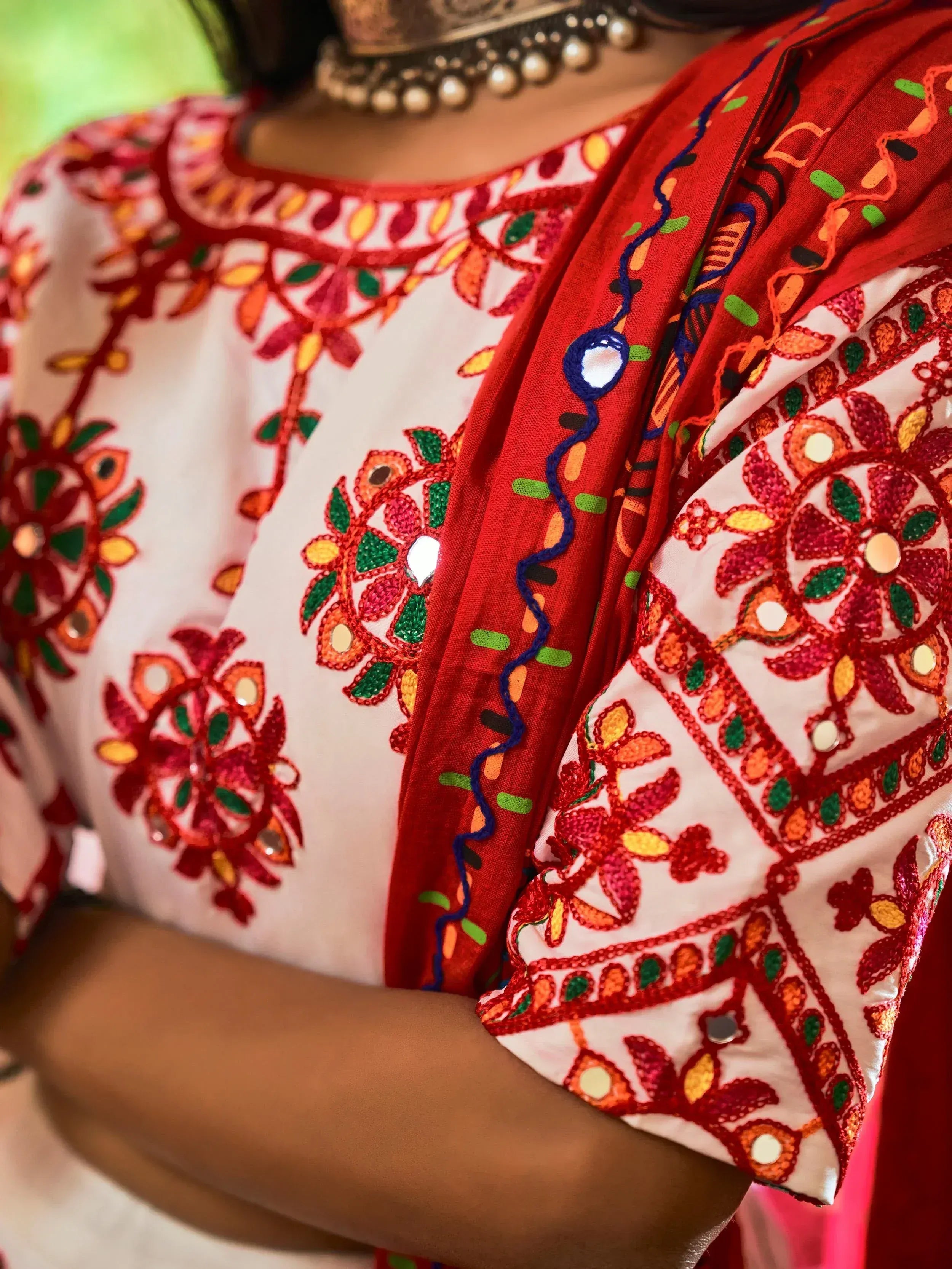 White and red embroidered ethnic top with mirror work and floral patterns, paired with traditional jewelry