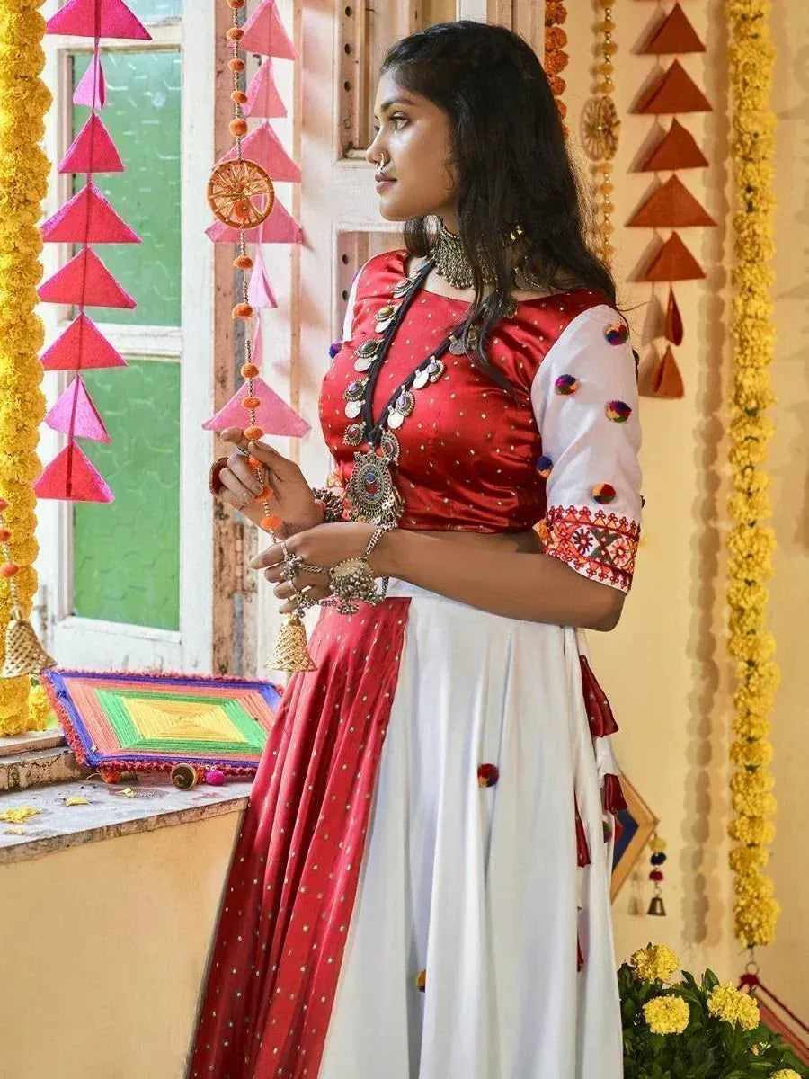 Red and white ethnic lehenga choli with mirror work, pom-poms, and traditional jewelry, festive Indian wear