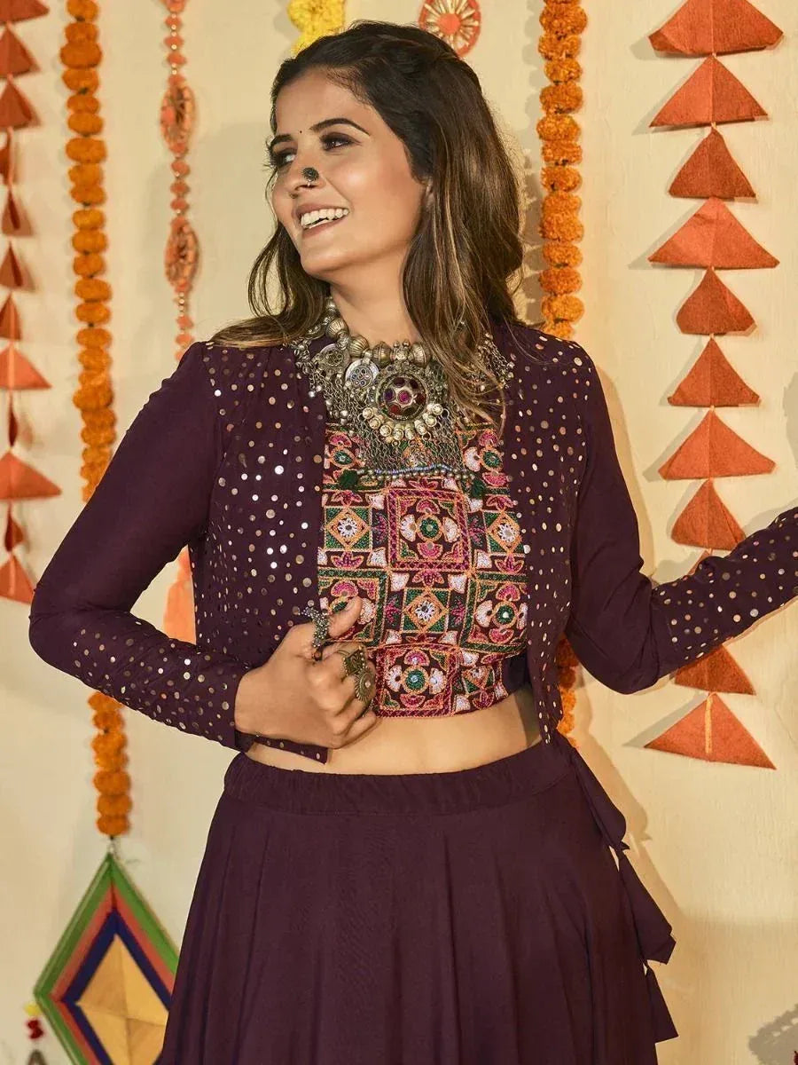 Woman in purple embroidered crop top and skirt, festive Indian ethnic wear with mirror work and jewelry