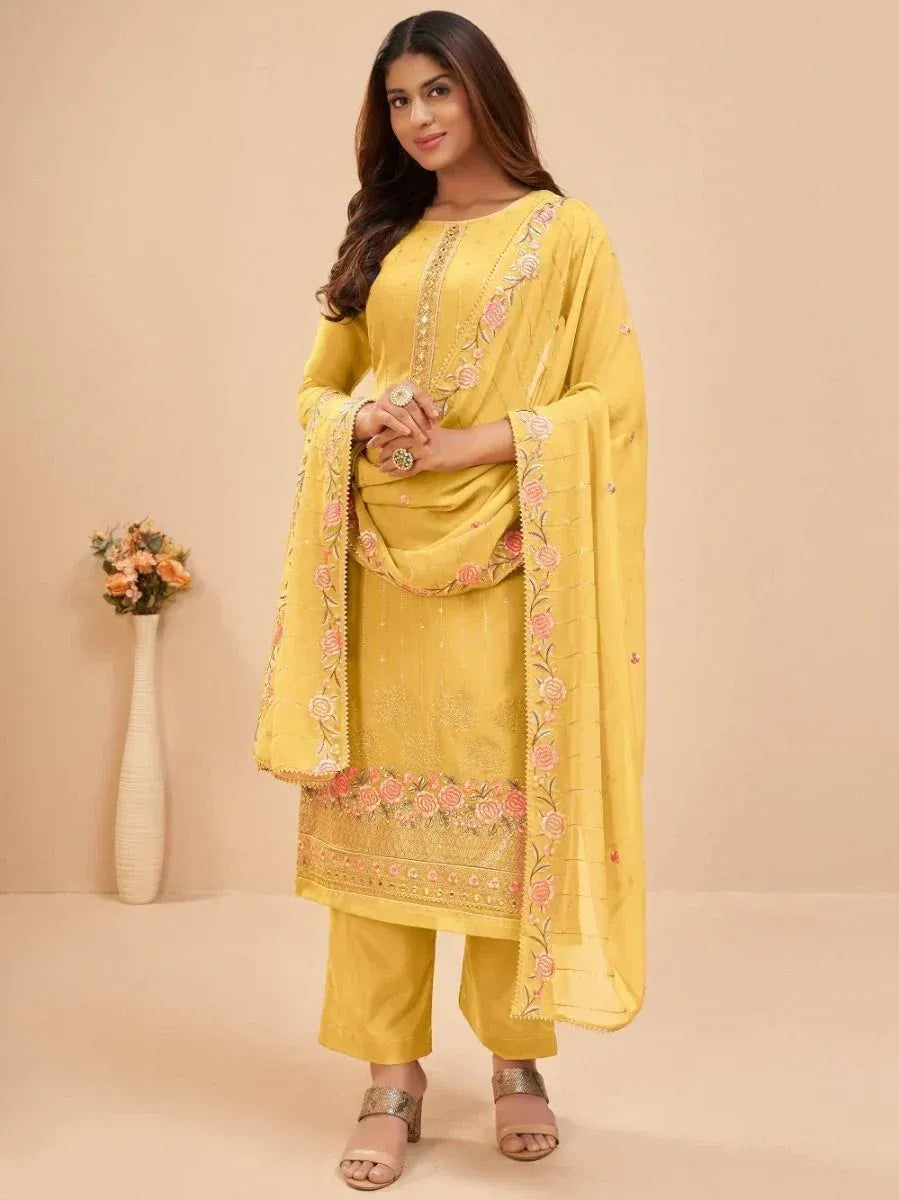 Woman in yellow embroidered salwar kameez with matching dupatta, standing indoors
