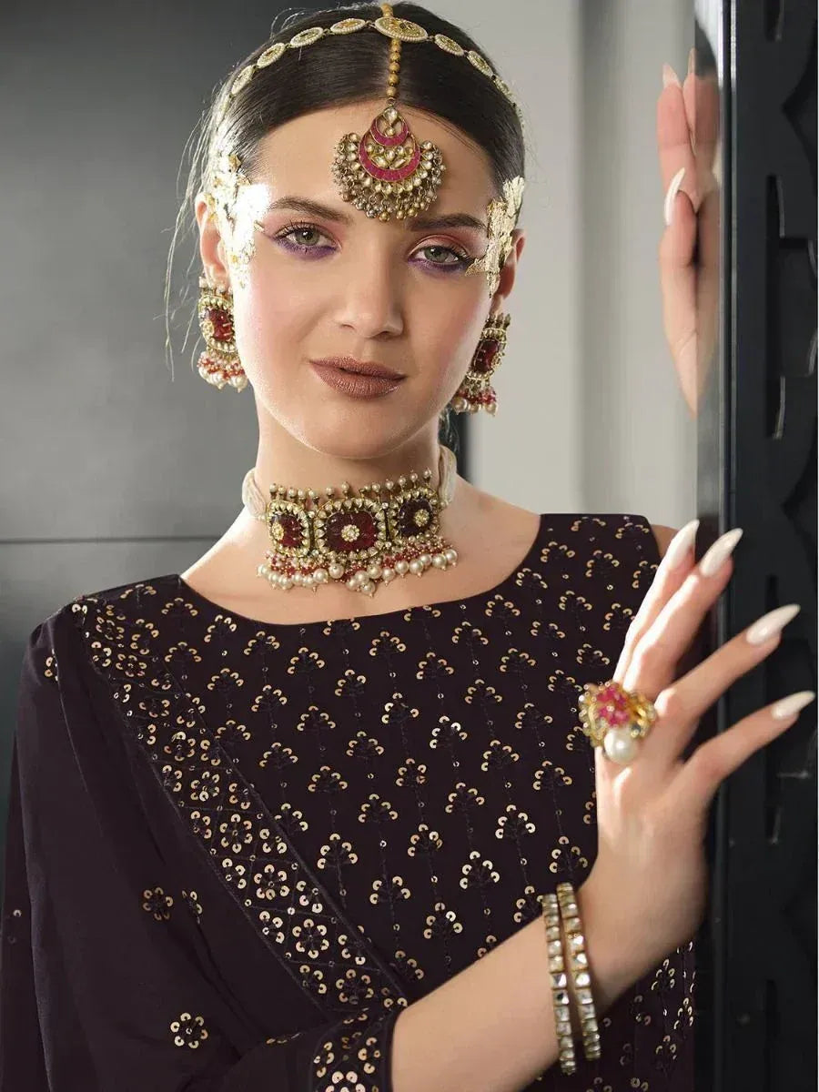 Woman in black embroidered ethnic gown with gold jewelry and maang tikka, perfect for Indian weddings or festivals.