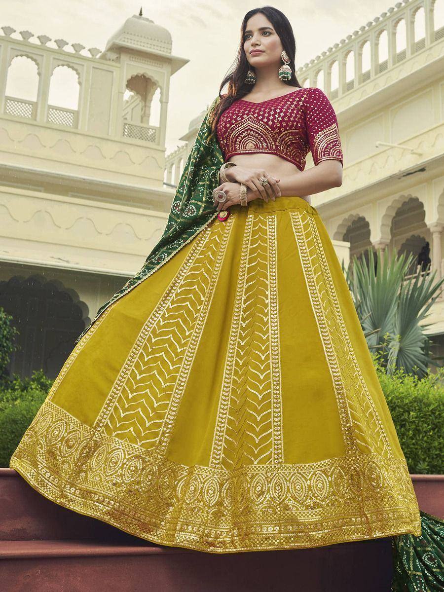 Woman in maroon blouse and mustard yellow lehenga with gold embroidery, paired with green dupatta, at palace backdrop