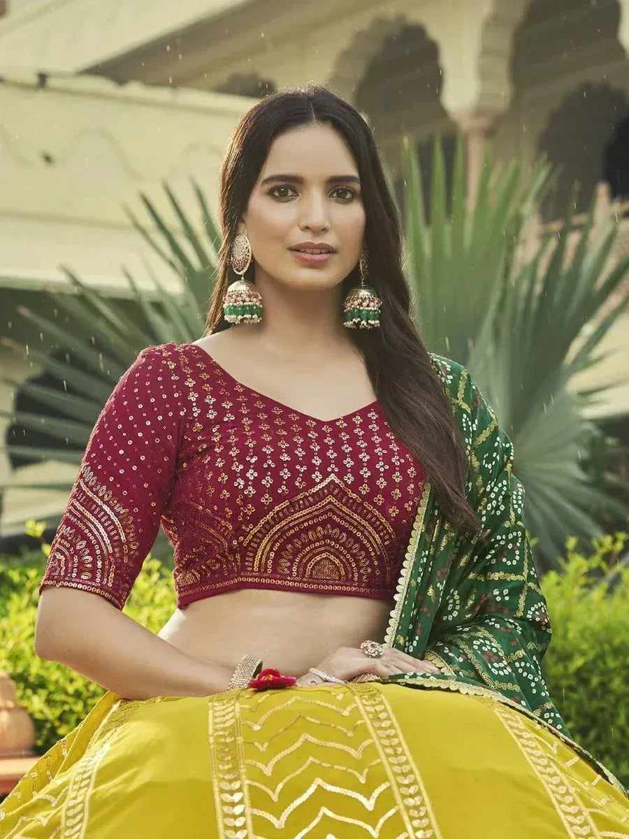 Woman in maroon embroidered blouse, yellow lehenga, and green dupatta, styled with jhumka earrings for ethnic wear.