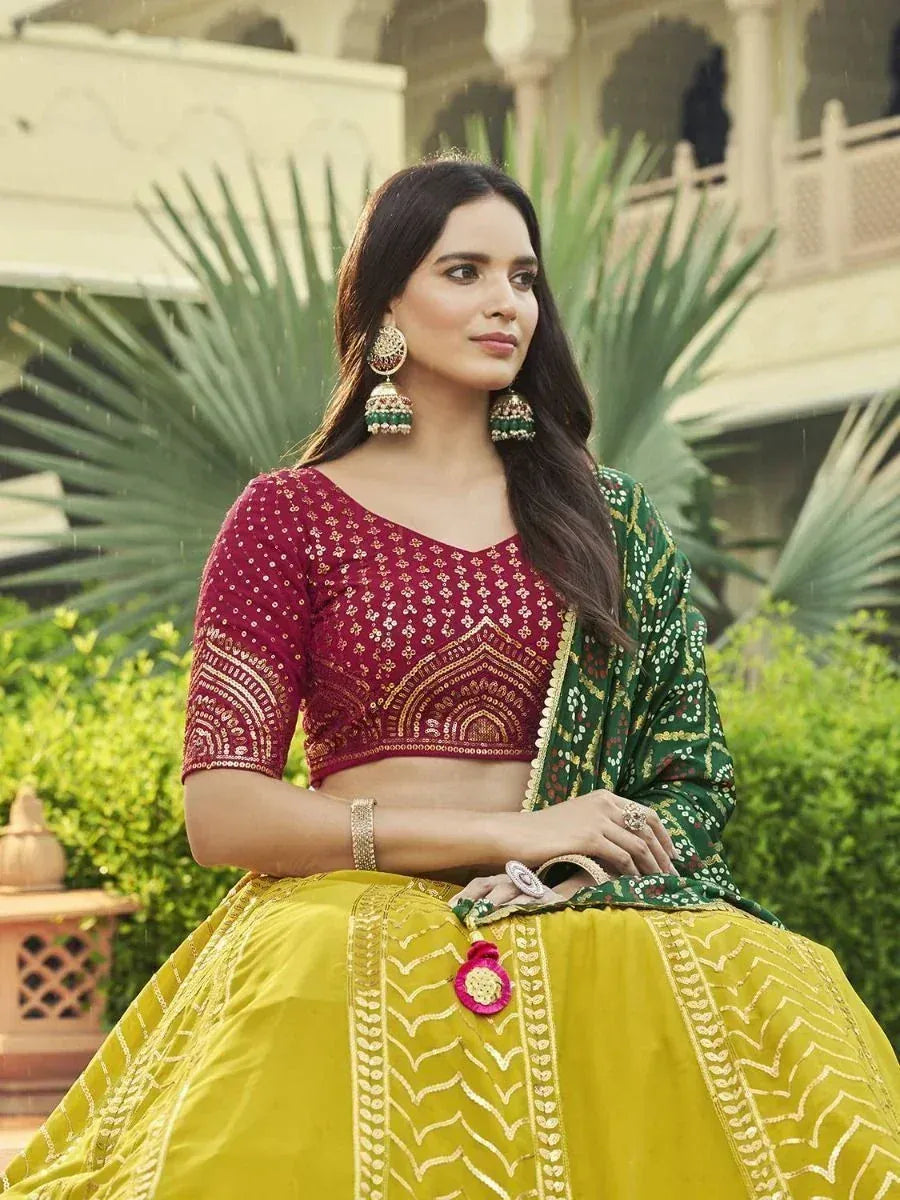 Woman in maroon embroidered blouse, yellow lehenga, and green dupatta, styled with jhumka earrings for ethnic wear.